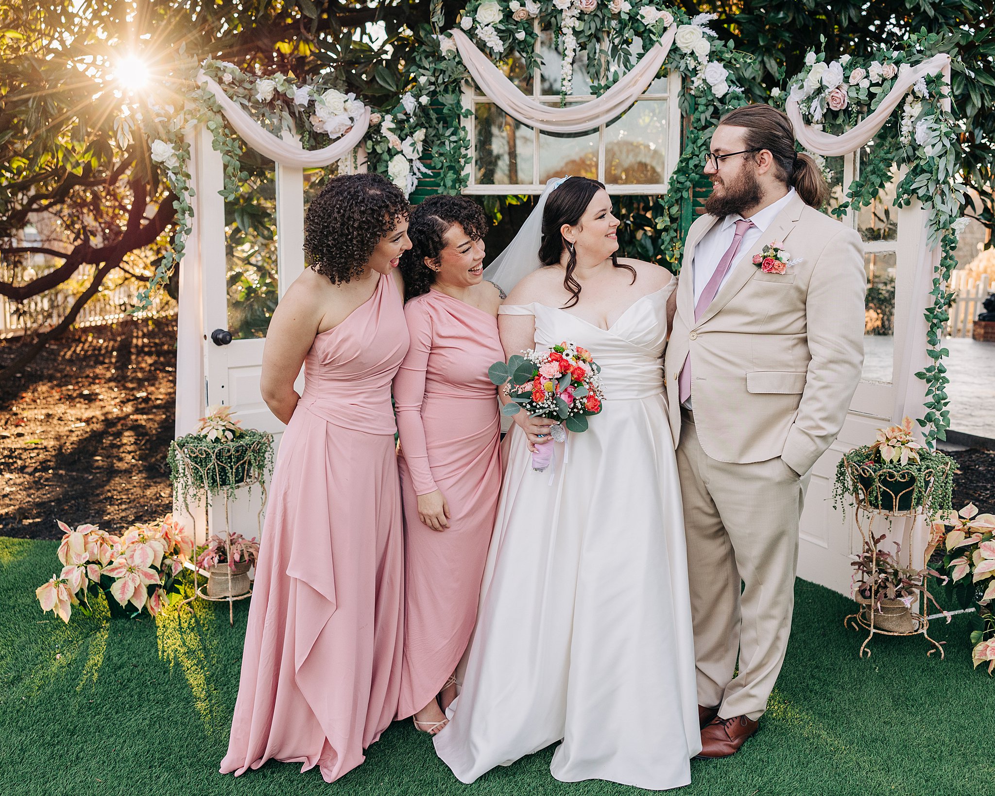 A bride stands in a garden ceremony location with her bridesmaids and brother