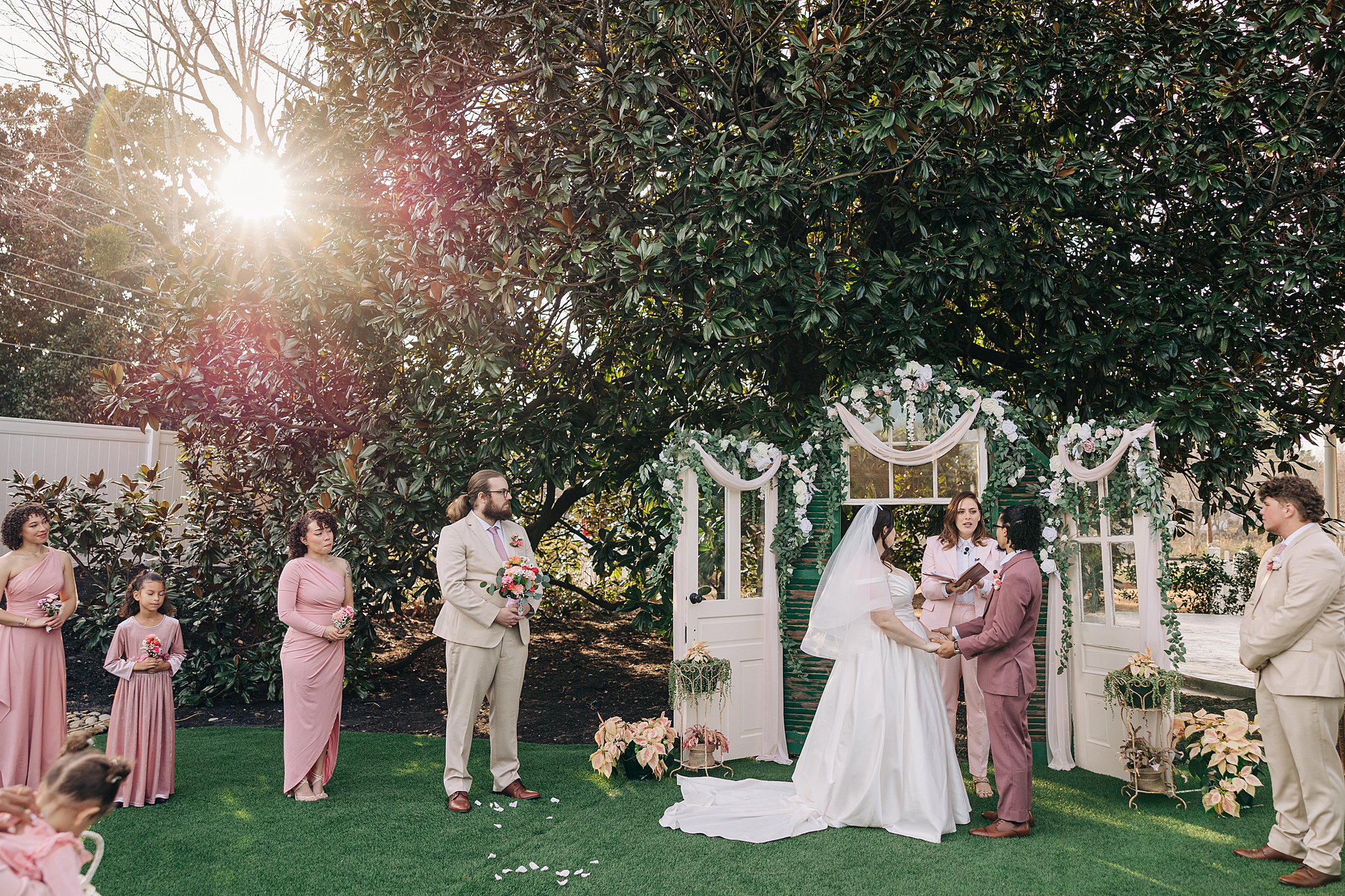 Newlyweds stand holding hands at sunset under a large Magnolia tree during their ceremony