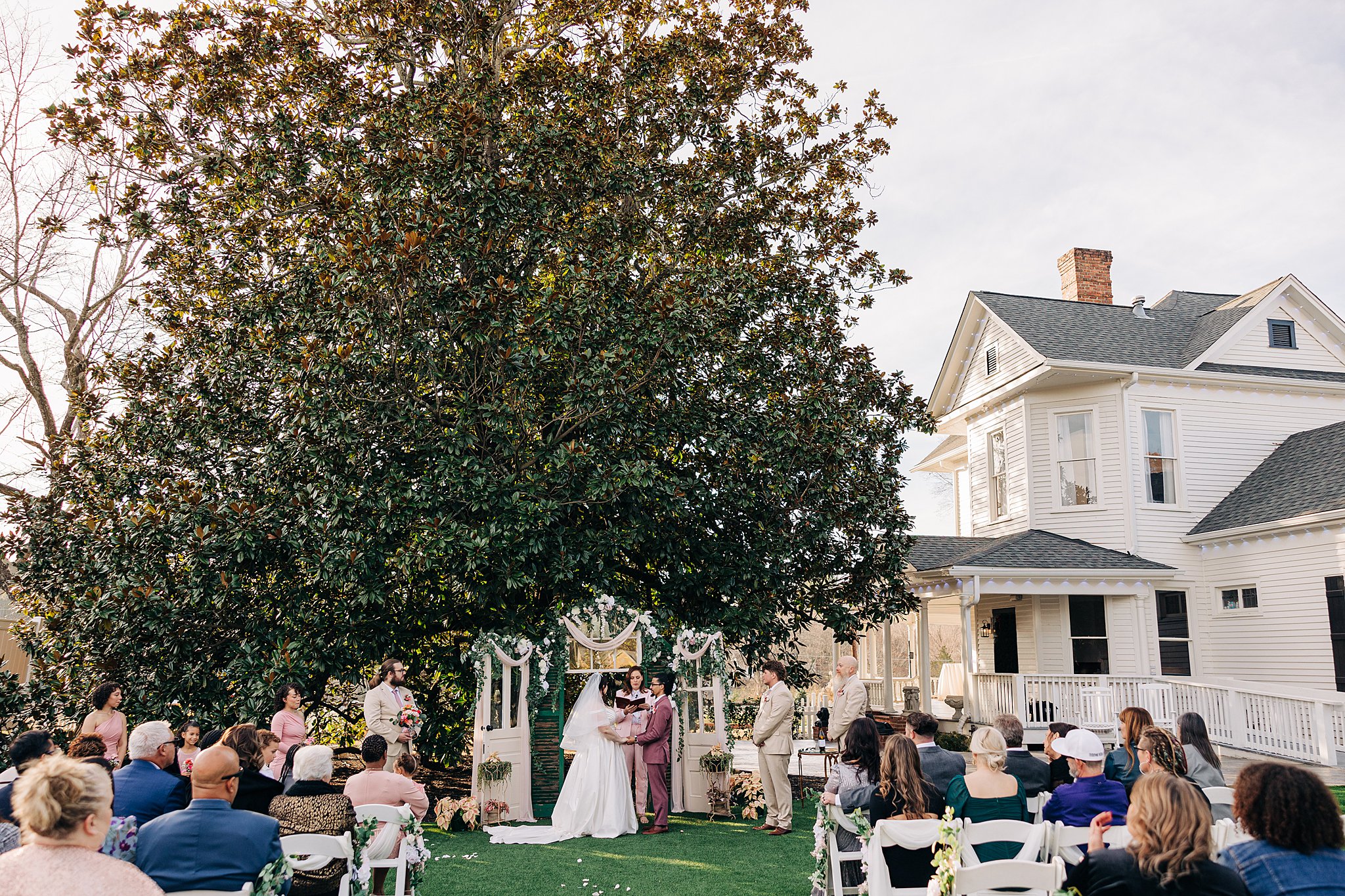 Newlyweds stand at the altar under a large magnolia tree at The Victorian: Youngsville
