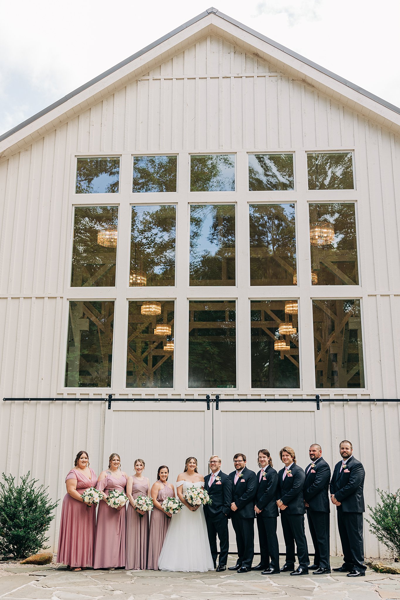 Newlyweds stand with their wedding party outside the main barn door entrance to carolina grove wedding venue