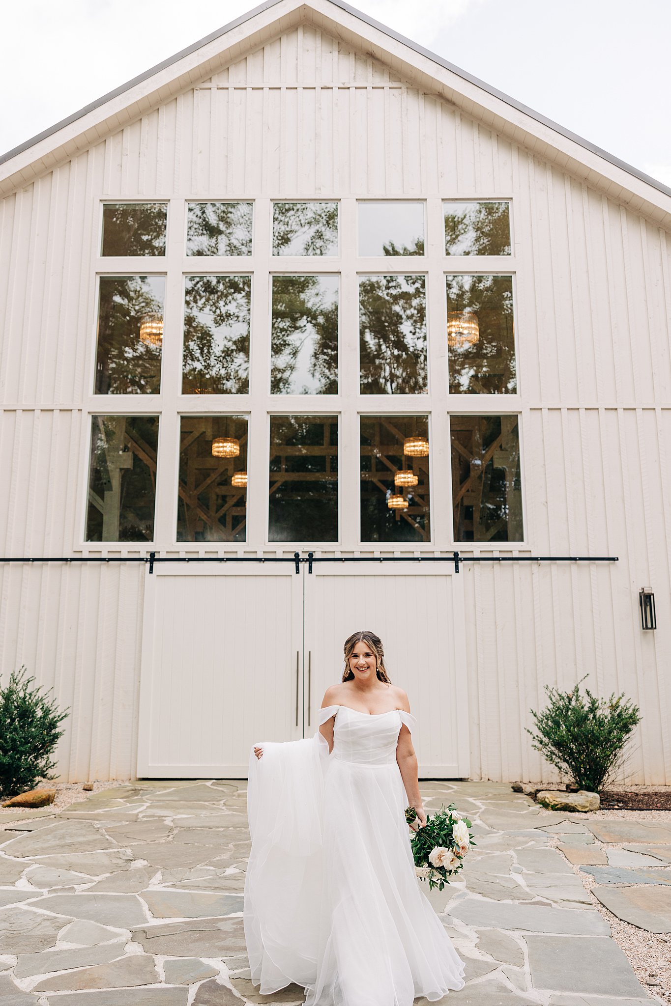 A bride holds her long train while walking on the stone patio at the carolina grove wedding venue