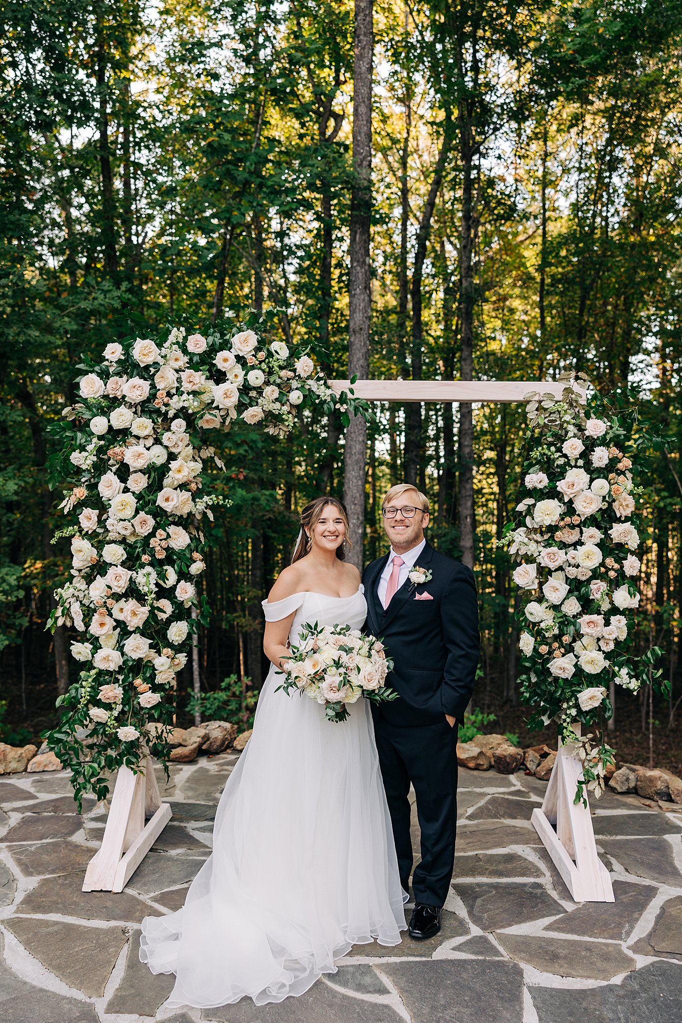 NEwlyweds stand under their carolina grove wedding venue ceremony arbor on a stone patio in the woods