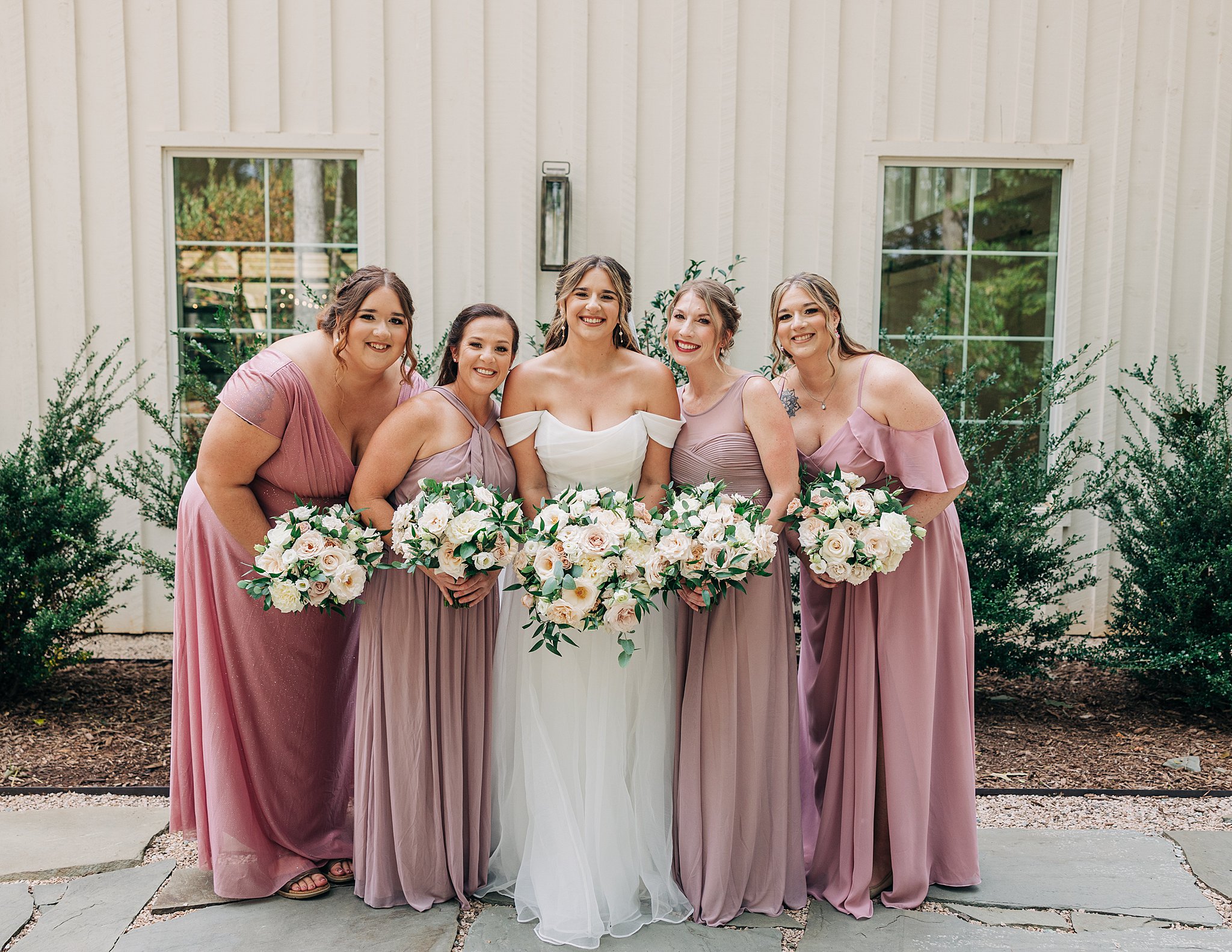 A bride smiles with her bridesmaids while holding their bouquets