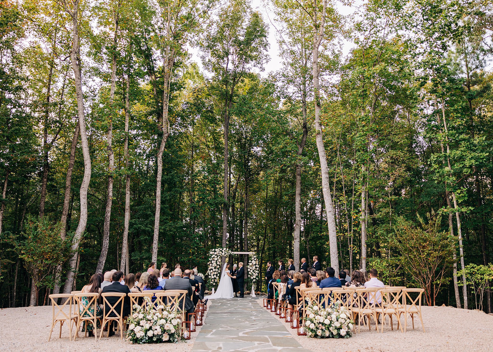 A wide look at an outdoor wedding ceremony in the forest at the carolina grove wedding venue
