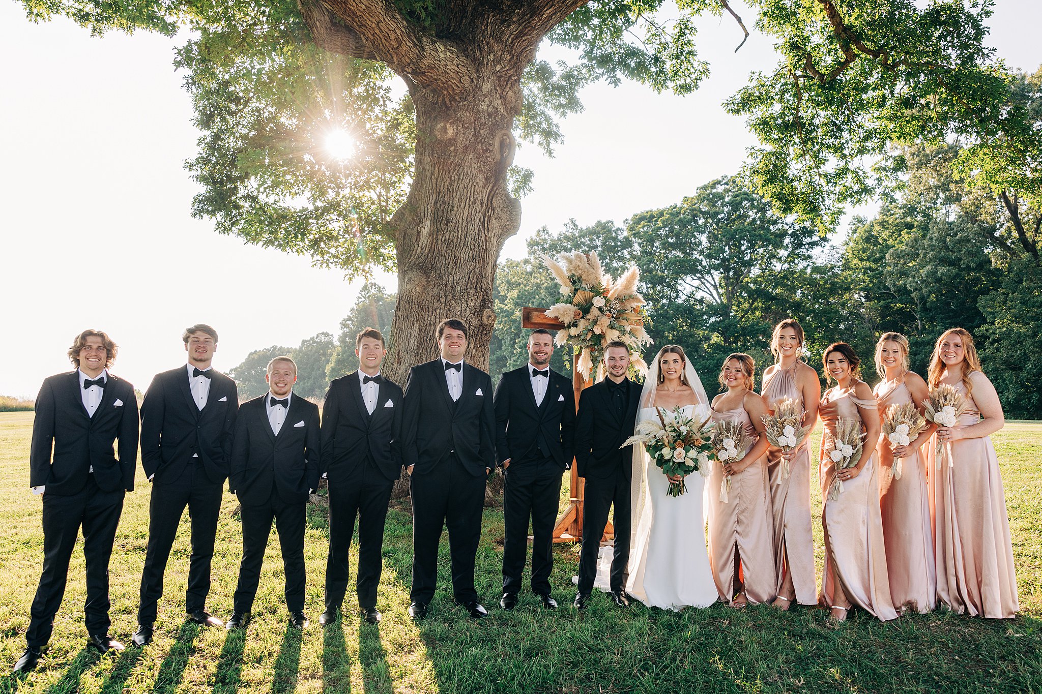 Newlyweds stand in a lawn smiling with their wedding party at their Summerfield Farms wedding