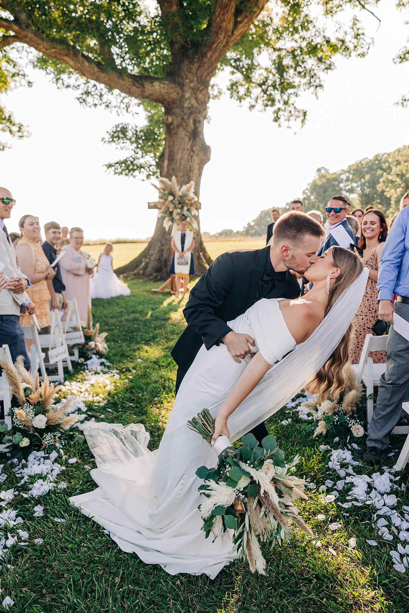 A groom dips his bride while exiting their Summerfield Farms wedding reception in the aisle with guests cheering them on