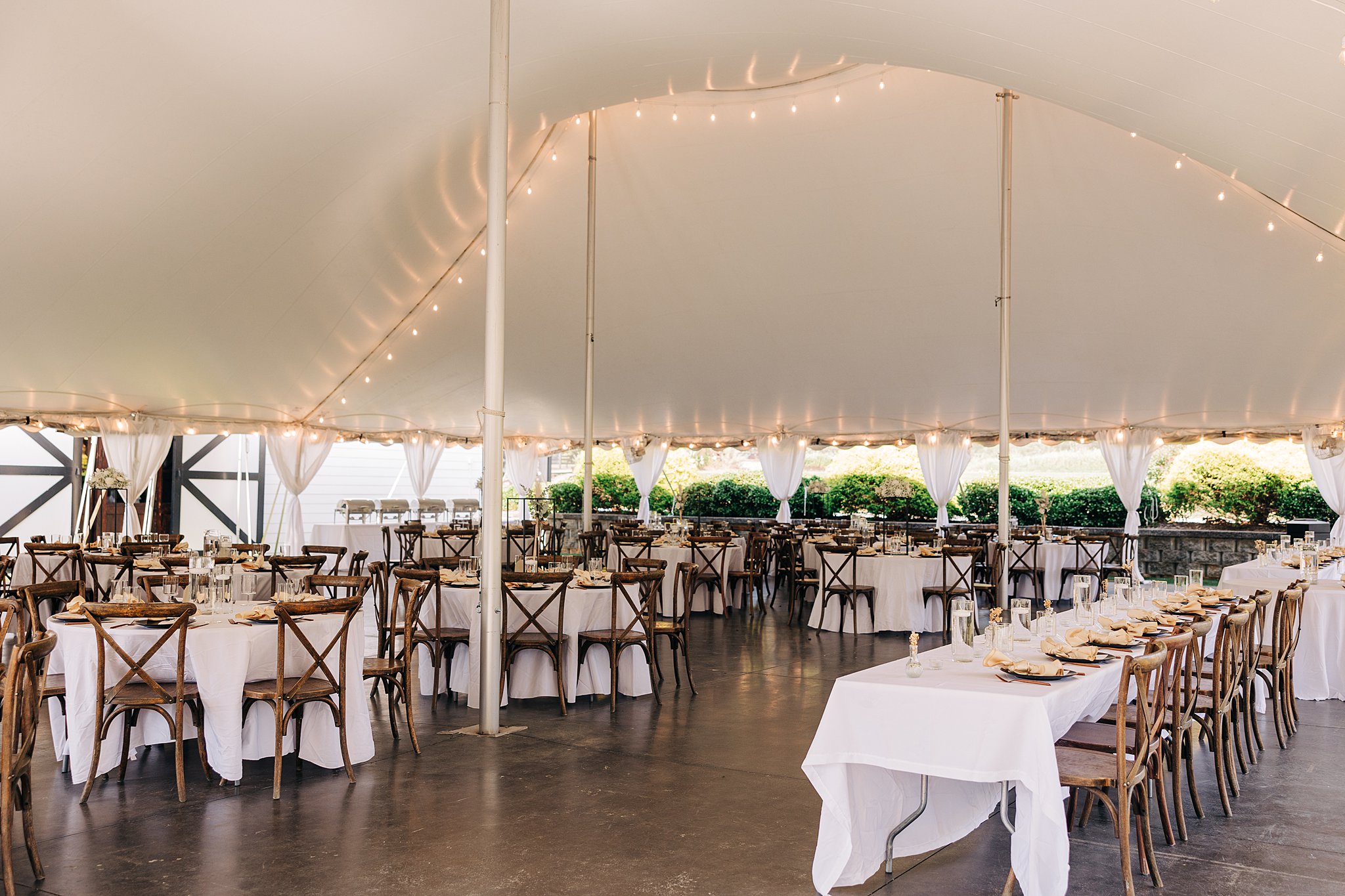 Details of an outdoor tent wedding reception set up with wooden chairs and market lights at the Summerfield Farms wedding venue