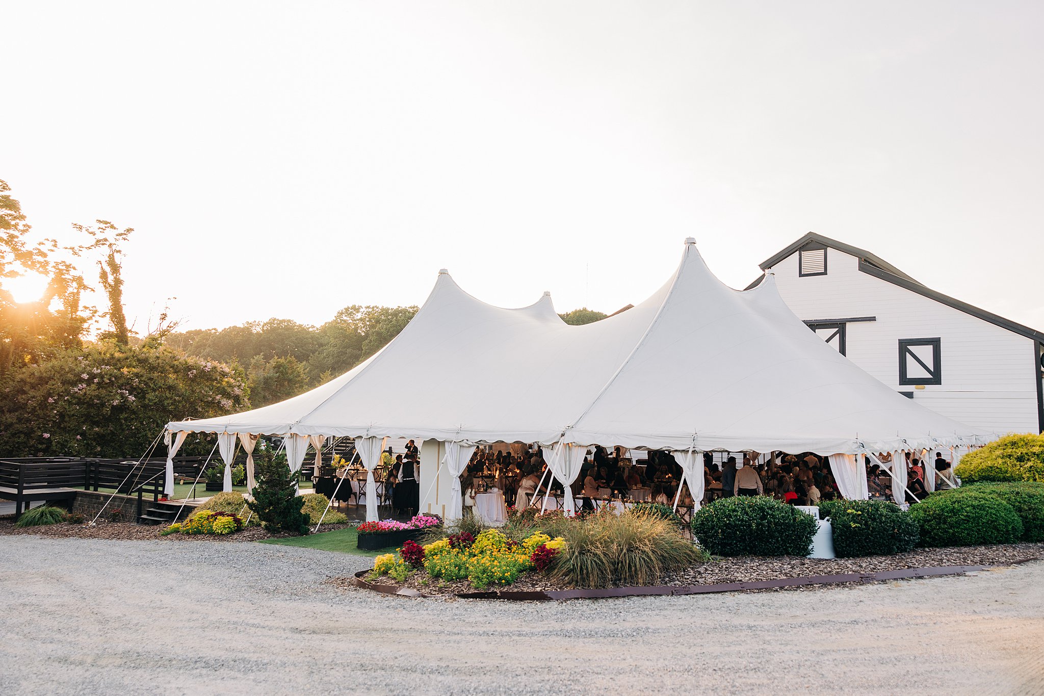 A view of a white wedding reception tent set up in a colorful garden at the Summerfield Farms wedding venue