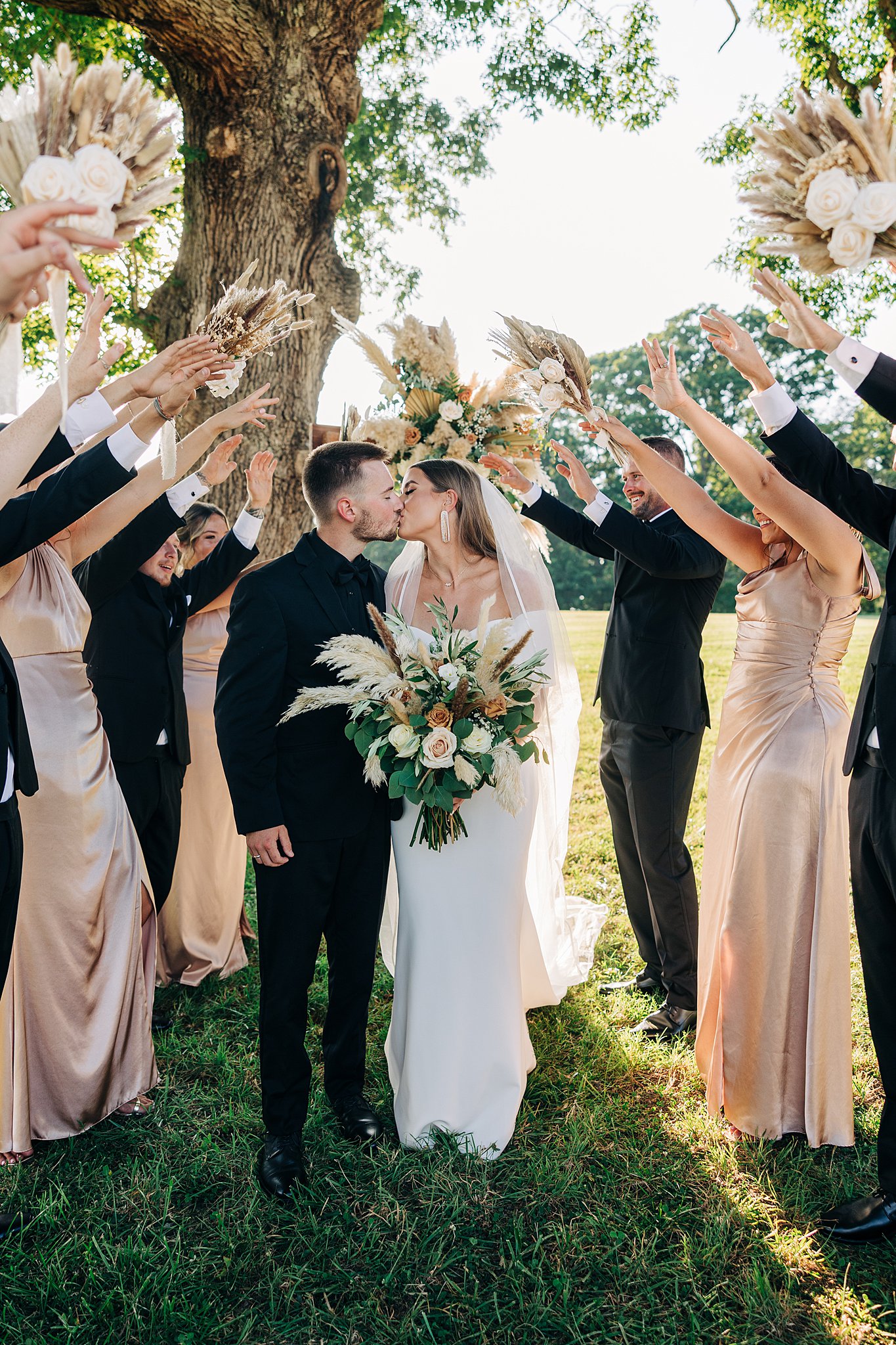 Newlyweds kiss while walking under their bridal party hands arch in a field