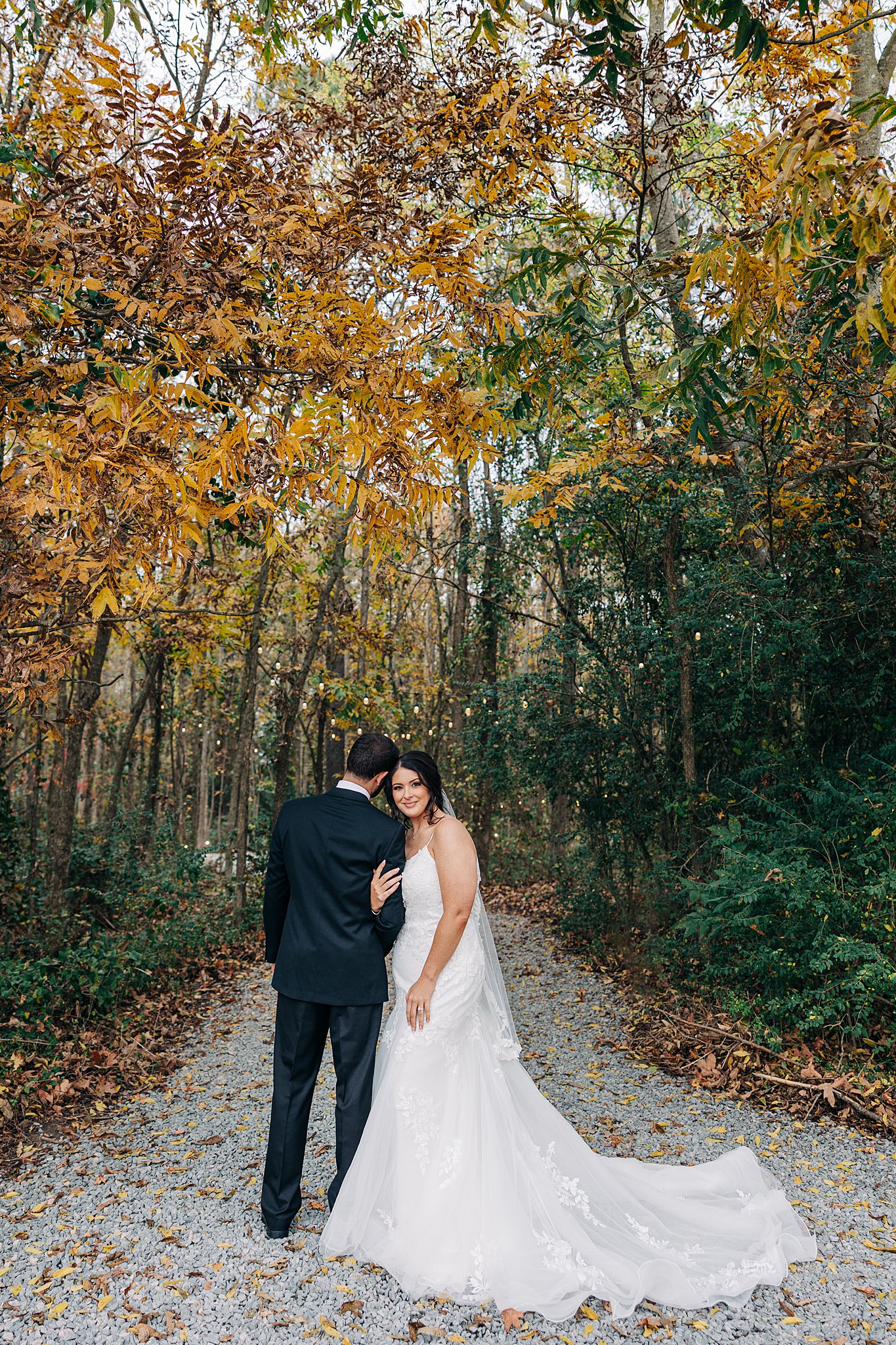 A bride hangs on the arm of her groom in a fall colored forest trail at their cornealius properties wedding