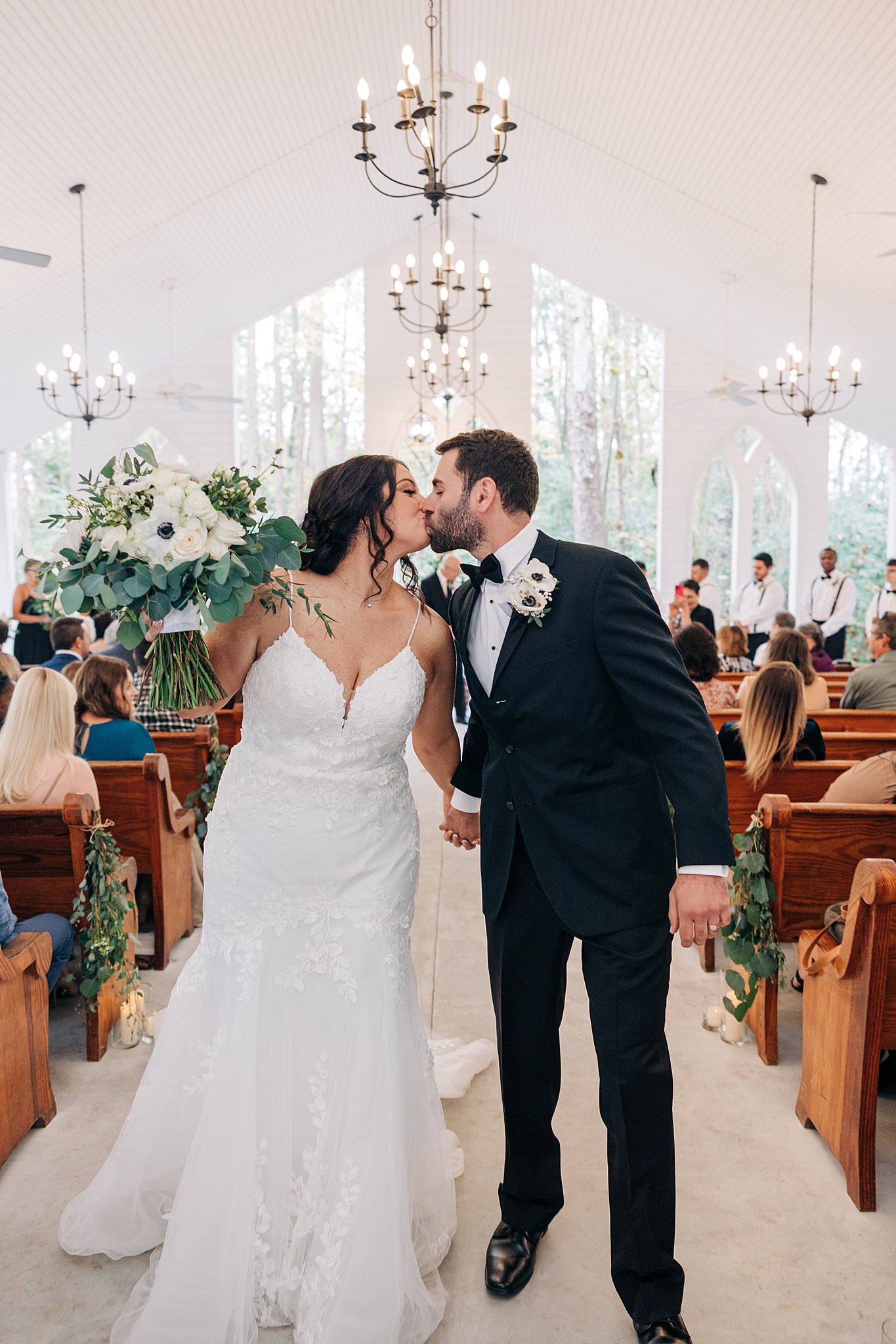Newlyweds kiss while exiting their wedding ceremony filled with guests