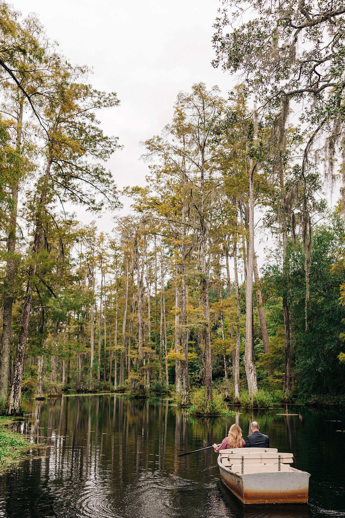A couple paddles through a river in a small boat during their cypress gardens wedding engagement