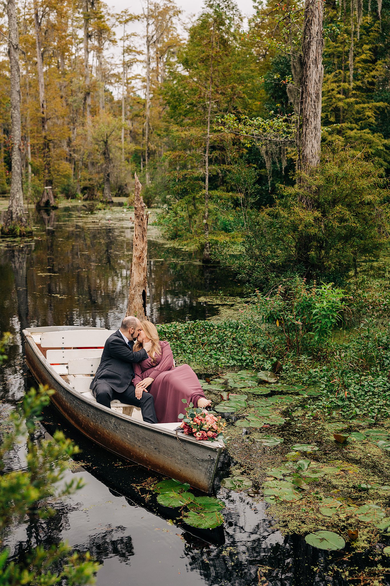 A couple in a small metal boat kiss while floating through the cypress swamp