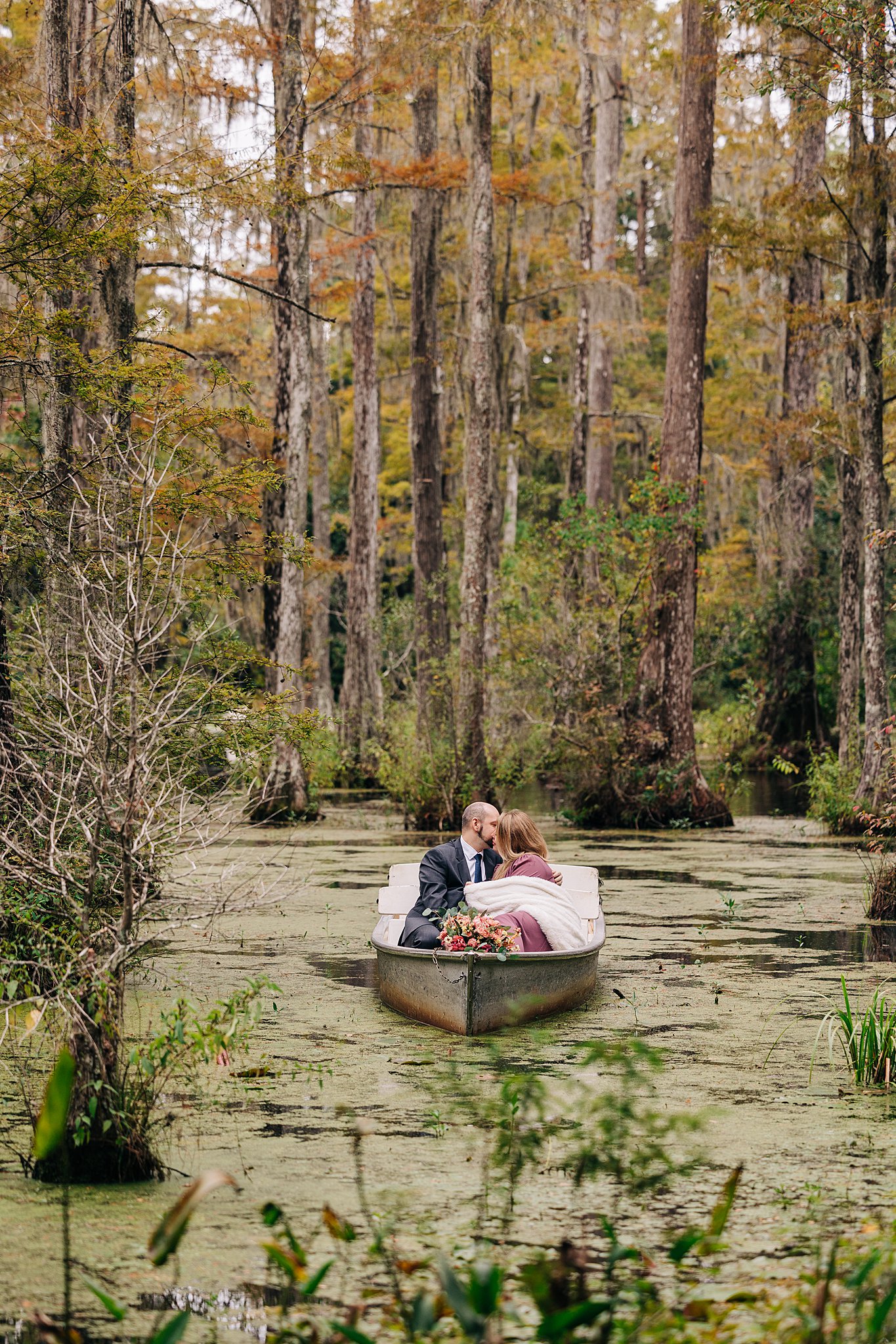 A couple enjoy a kiss while sitting in a boat during their cypress gardens wedding engagement