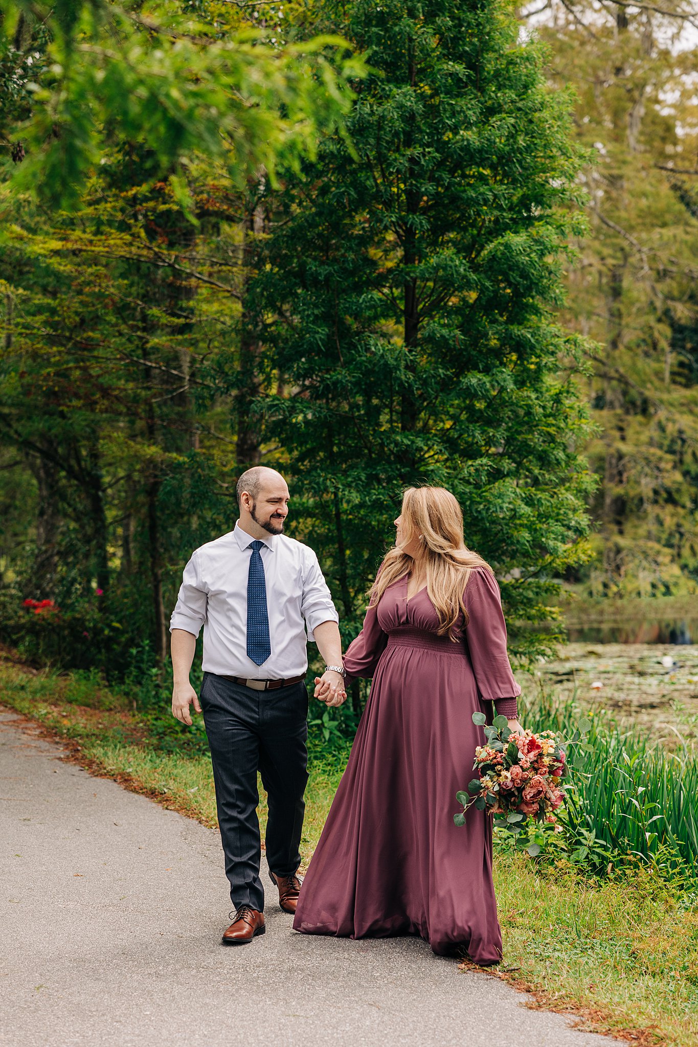 A newly engaged couple hold hands while walking through a park path during their cypress gardens wedding engagement
