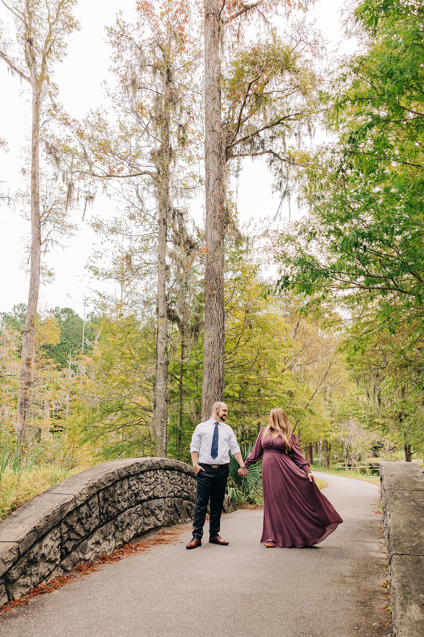 A newly engaged couple hold hands while walking across an old stone bridge walkway during their cypress gardens wedding engagement