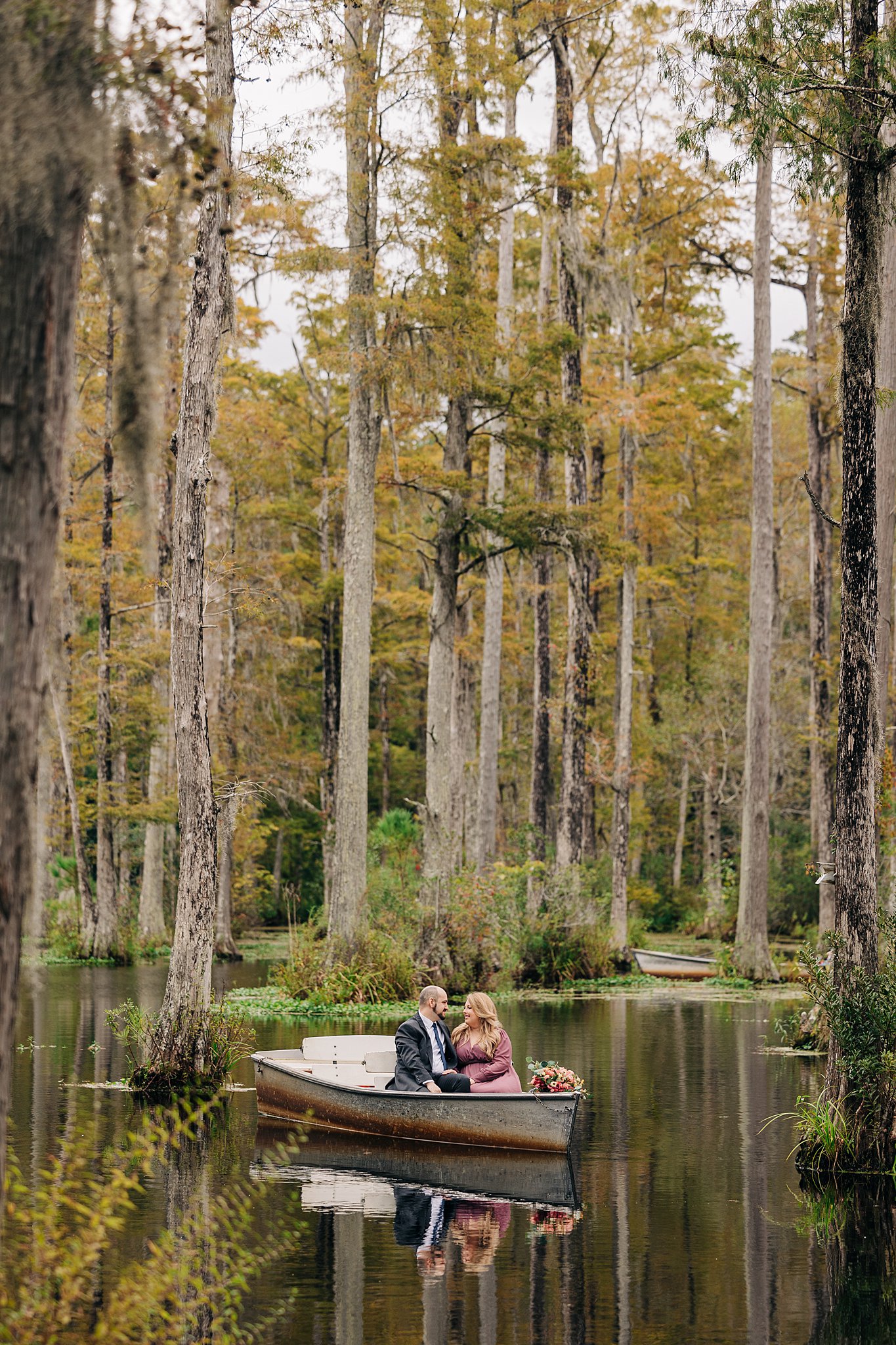 A couple in a small boat float through a swamp in a blue suit and pink dress