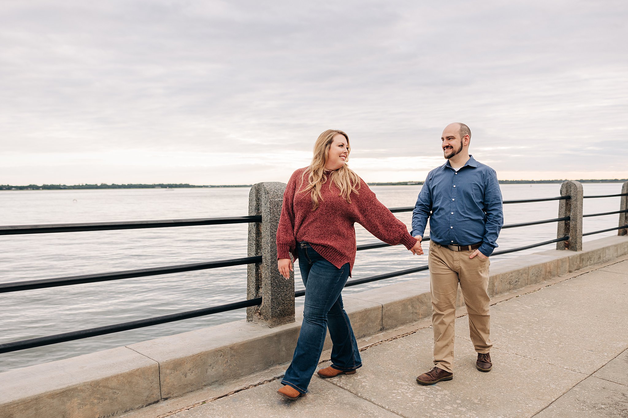 A woman in a red sweater leads her fiancee across a riverfront walkway