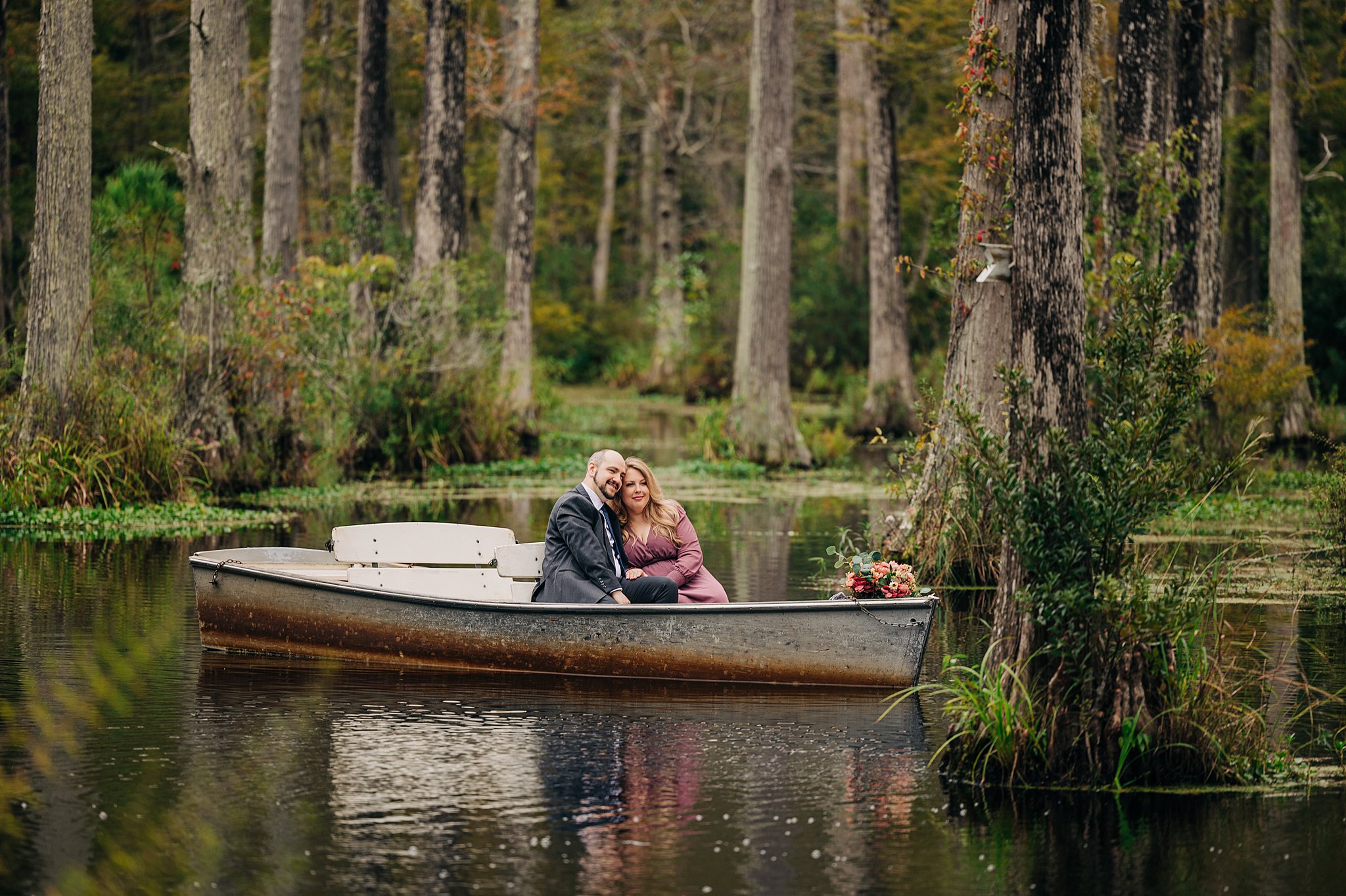 A couple in a suit and pink dress explore the waters in a boat during their engagement