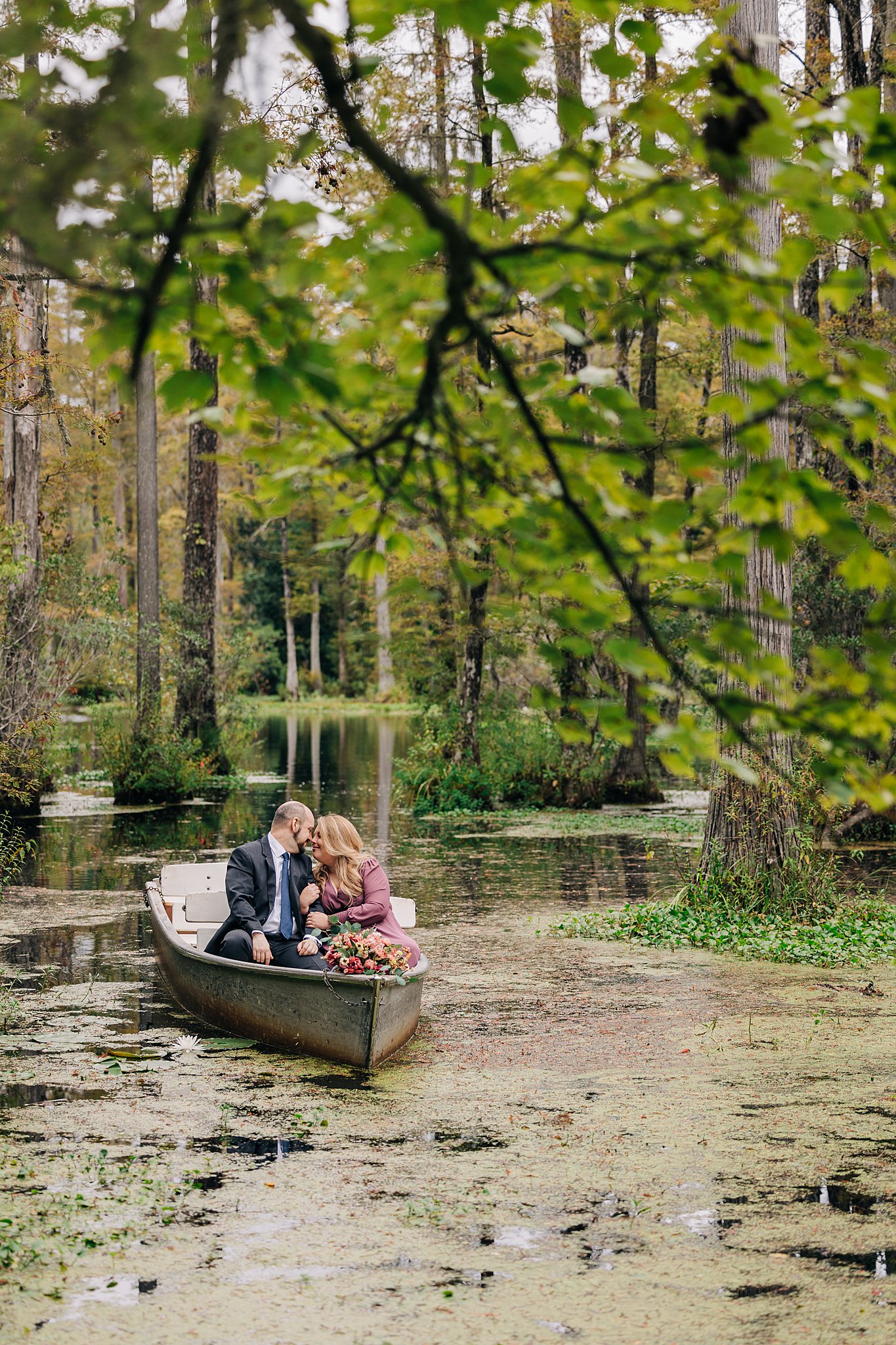 A young couple snuggle and lean in for a kiss while floating through a swamp during their engagement
