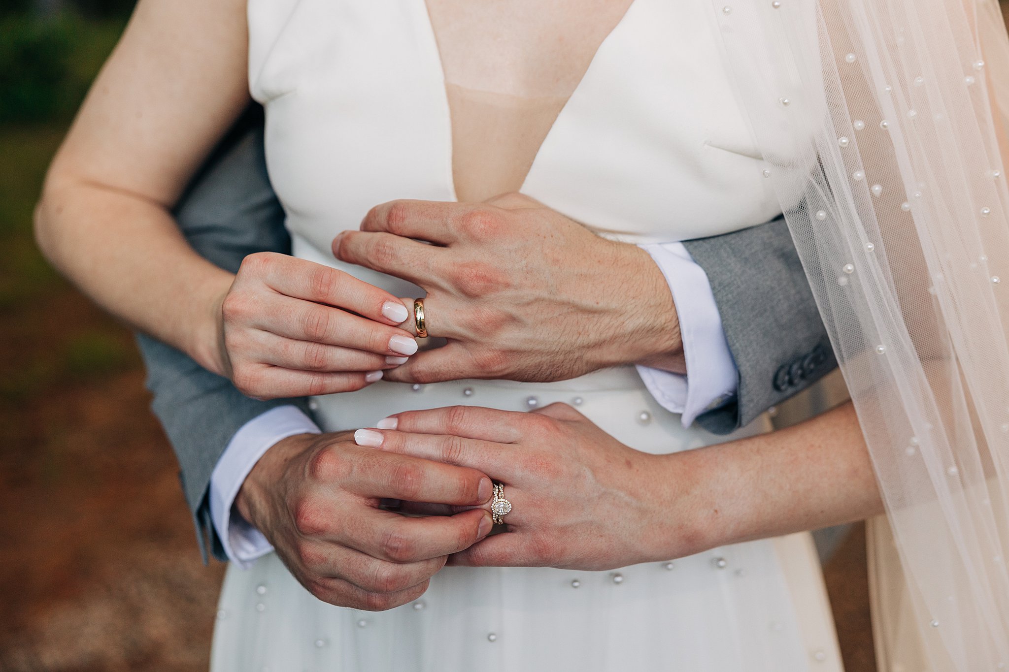 Details of newlyweds hold each other's ring fingers while standing outside