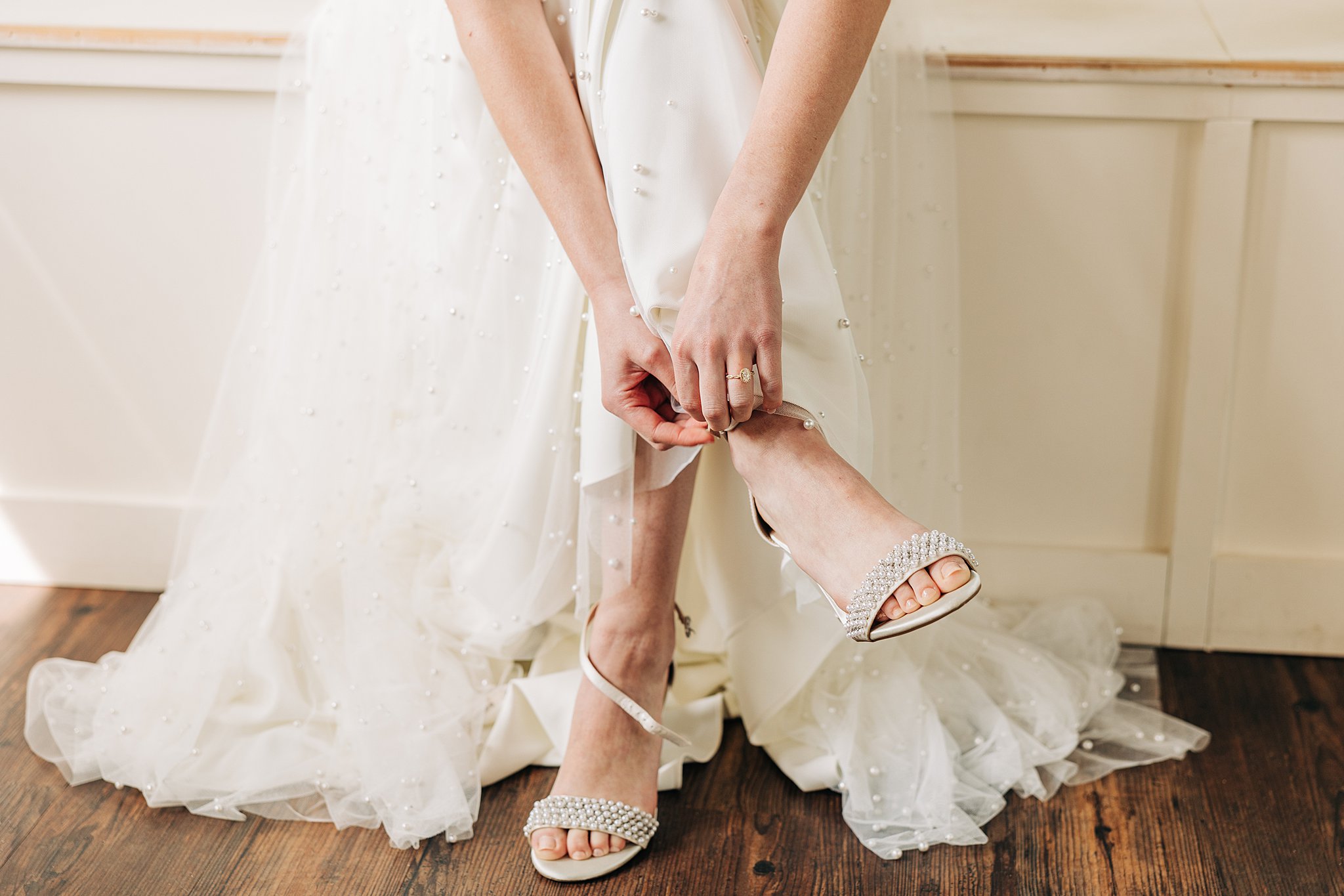 Details of a bride putting on her pearl covered shoes