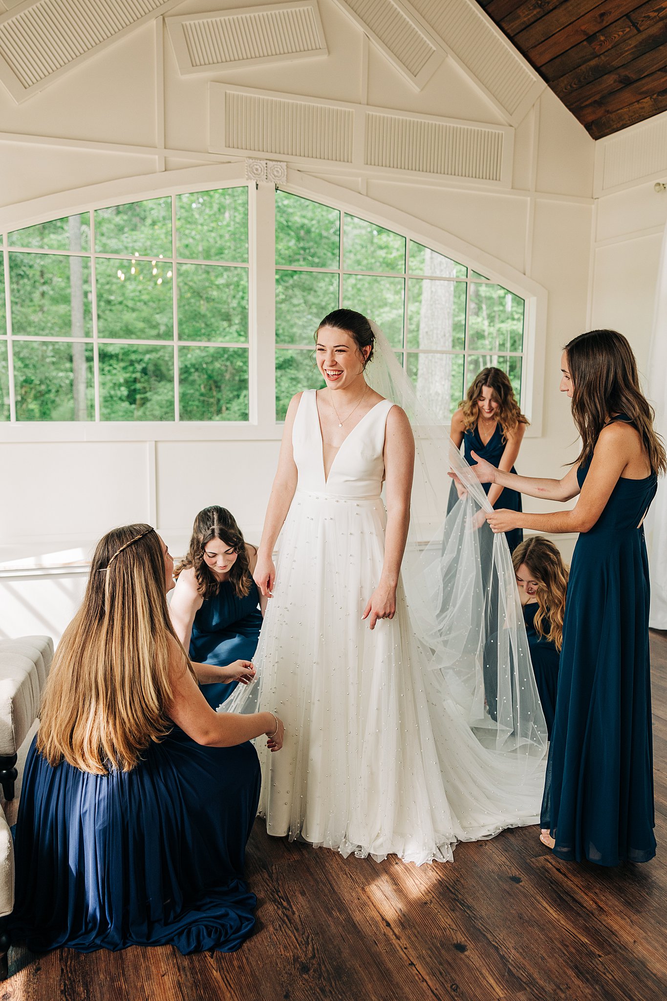 A happy bride stands in the center of a large room while her bridesmaids admire her dress at her pinehill pavilion wedding