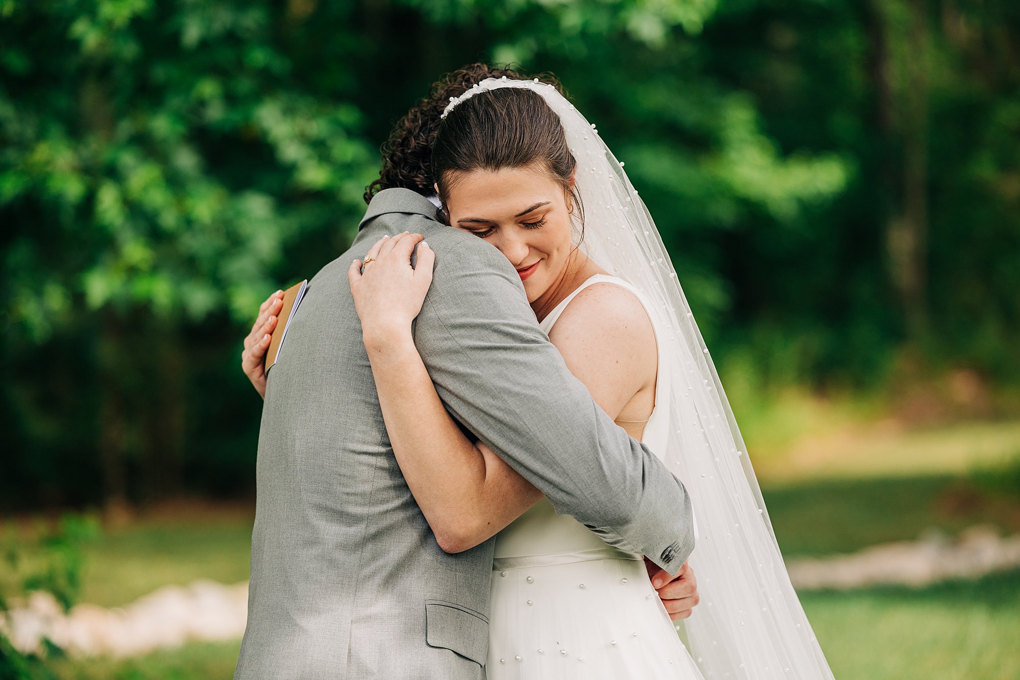Newlyweds share a happy hug while standing in a forest at their pinehill pavilion wedding