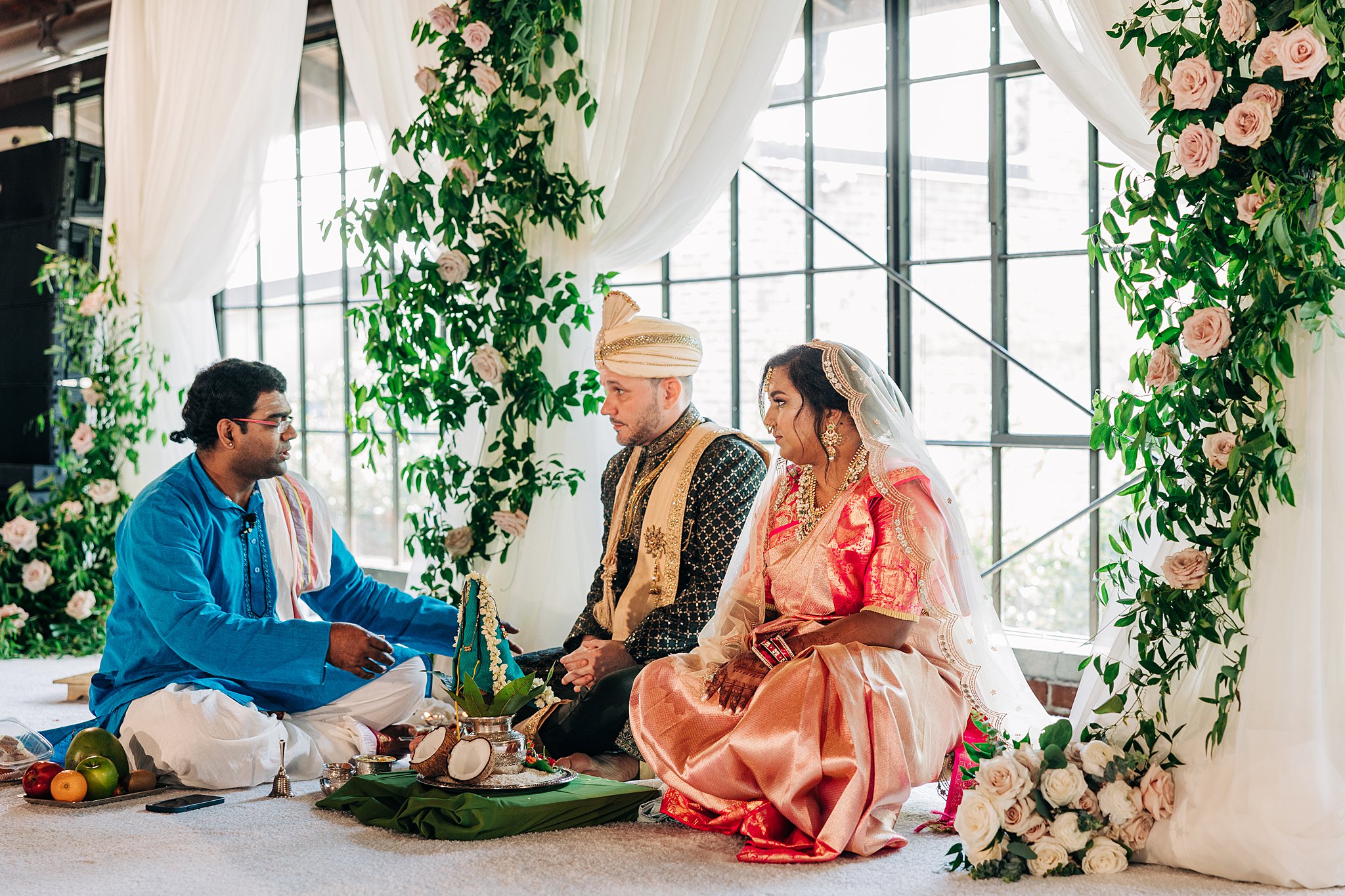 A bride and groom listen to their officiant during their traditional indian wedding