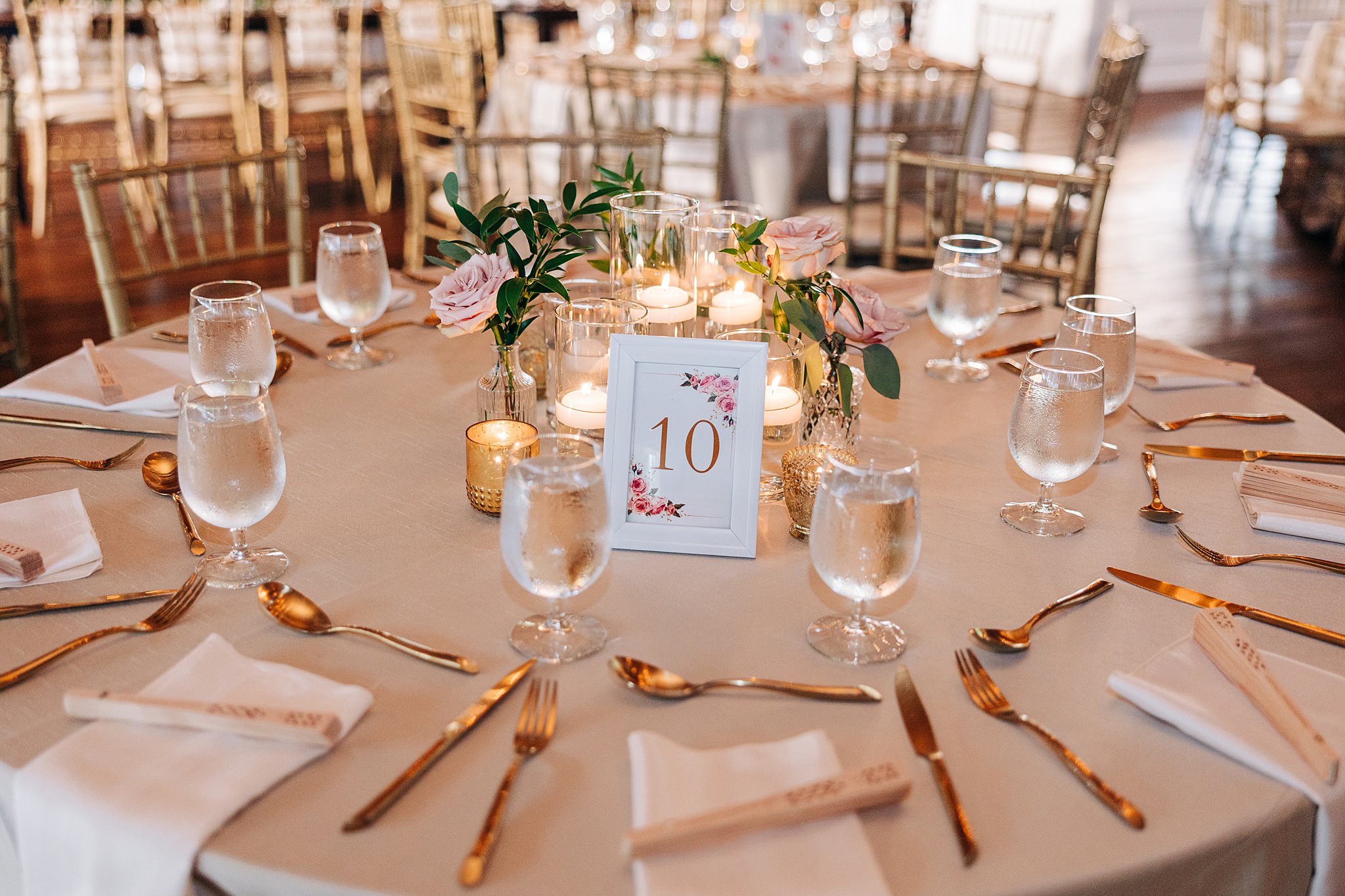 Details of a wedding reception table setting with gold silverware and candles