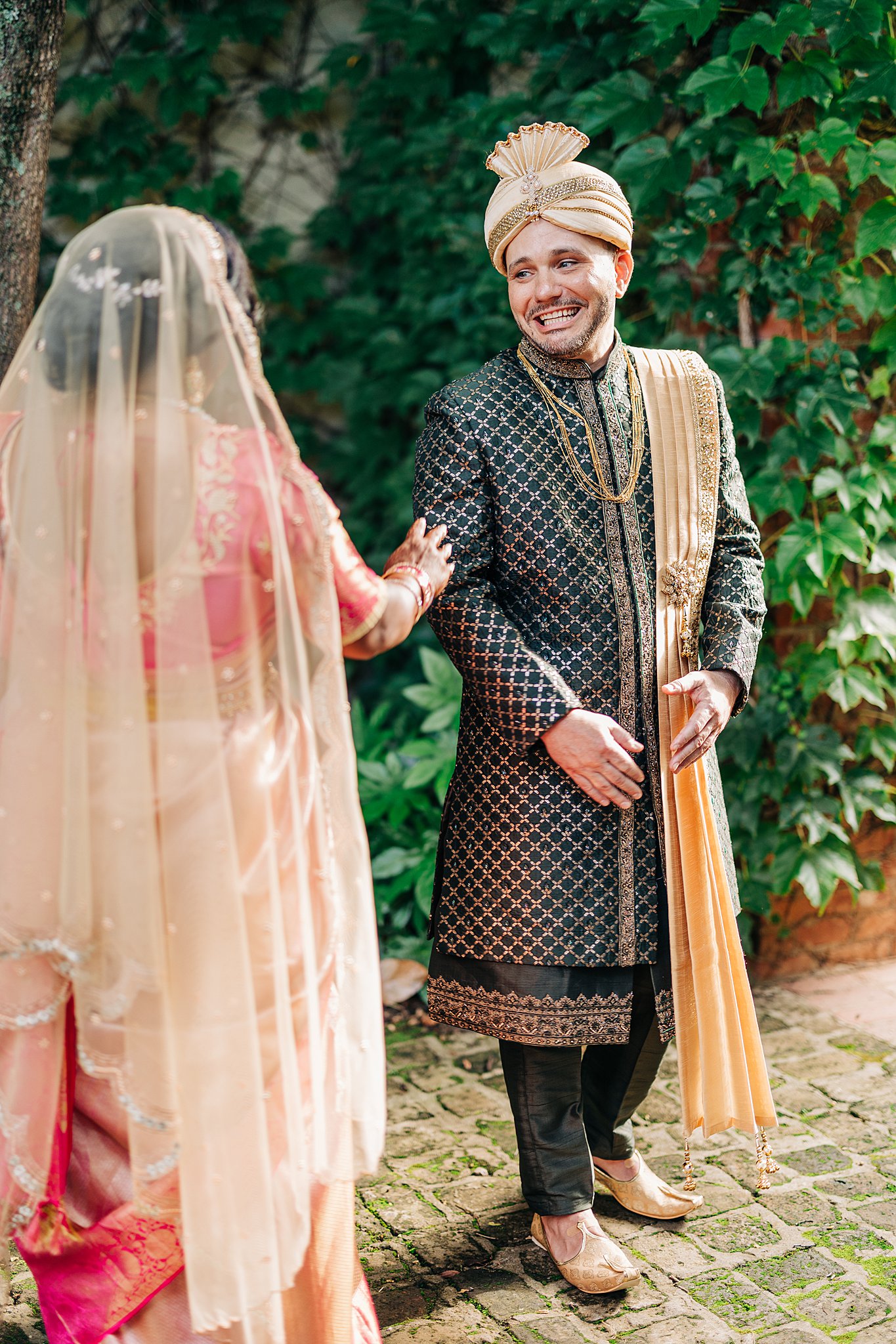 A groom smiles big during his first look with his bride in a pink traditional wedding dress