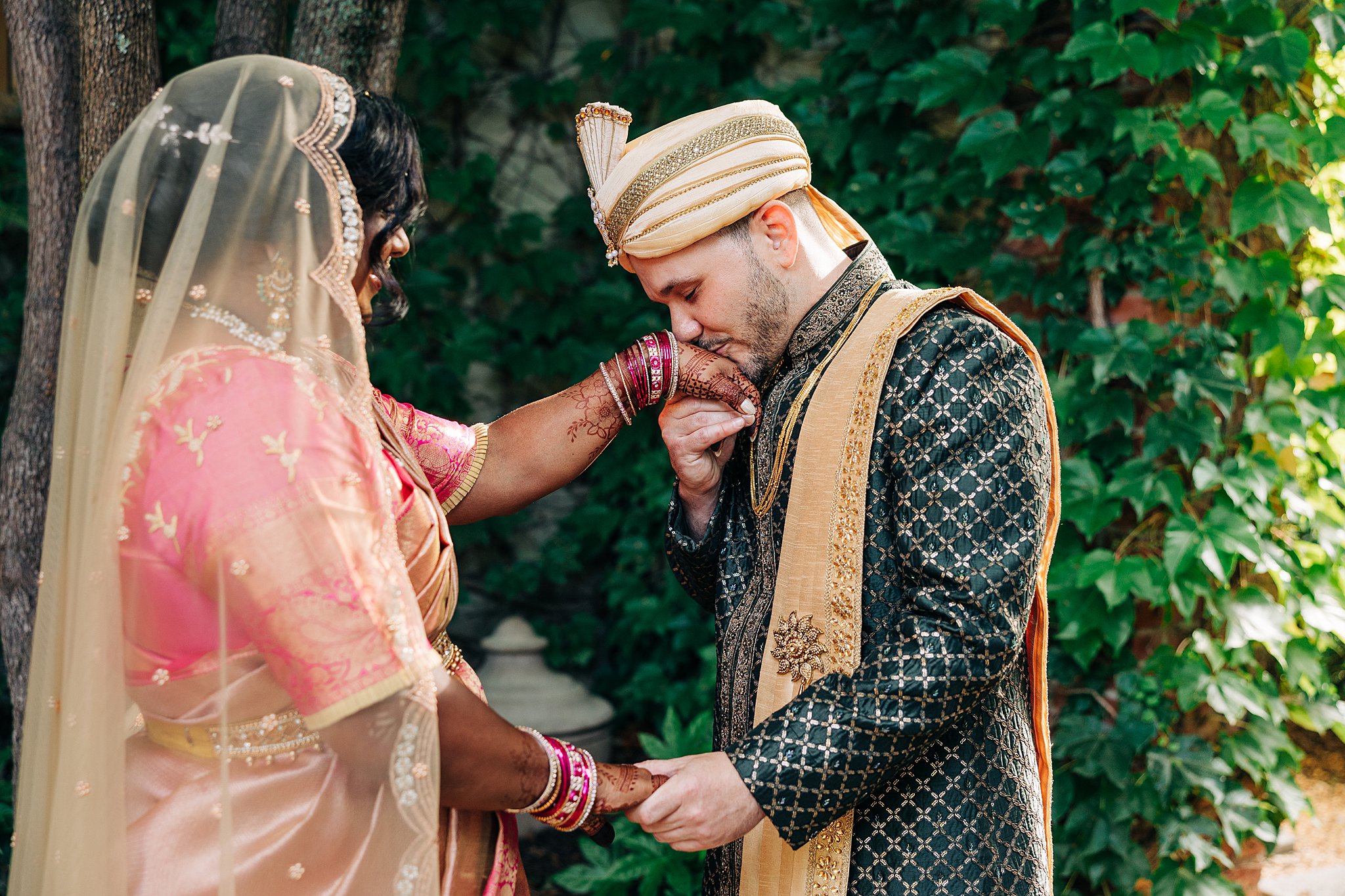 A groom kisses the henna covered hand of his bride in a garden at the summerour studio wedding venue