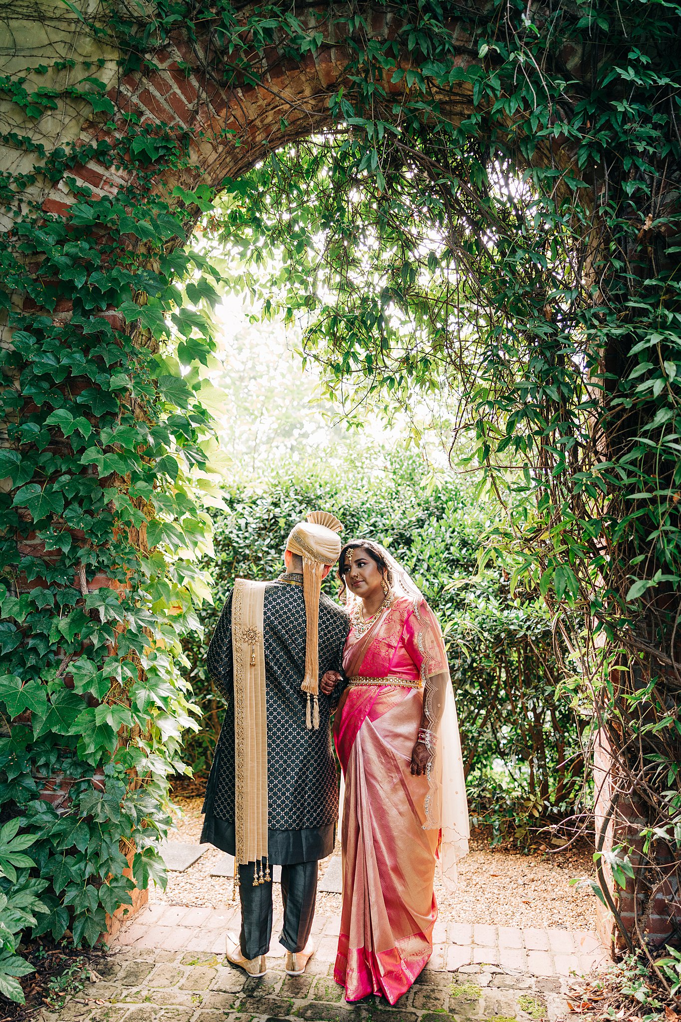 Newlyweds lean on each other under an ivy covered arch at their summerour studio wedding