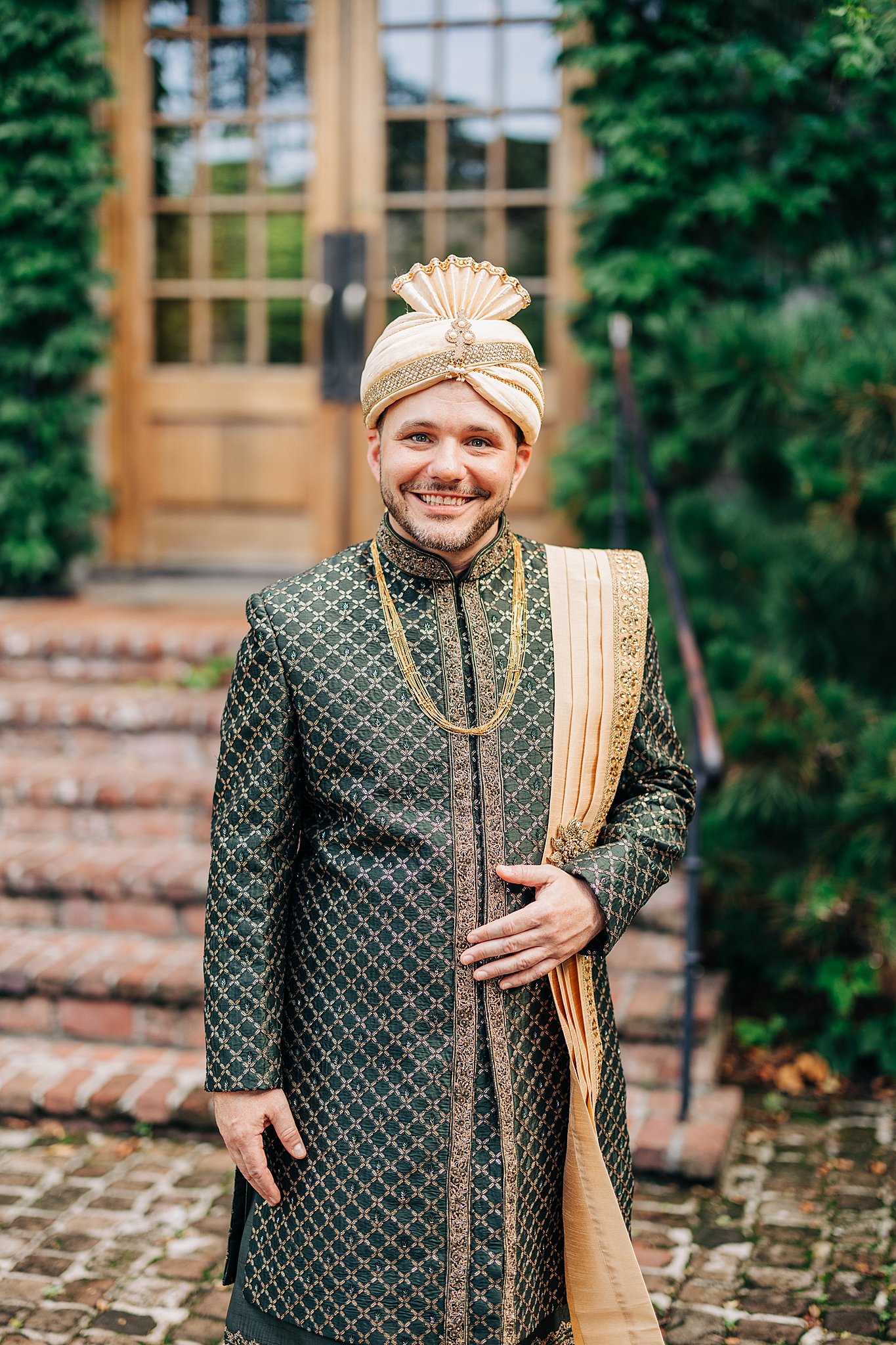 A groom in traditional indian wedding outfit stands in a garden path