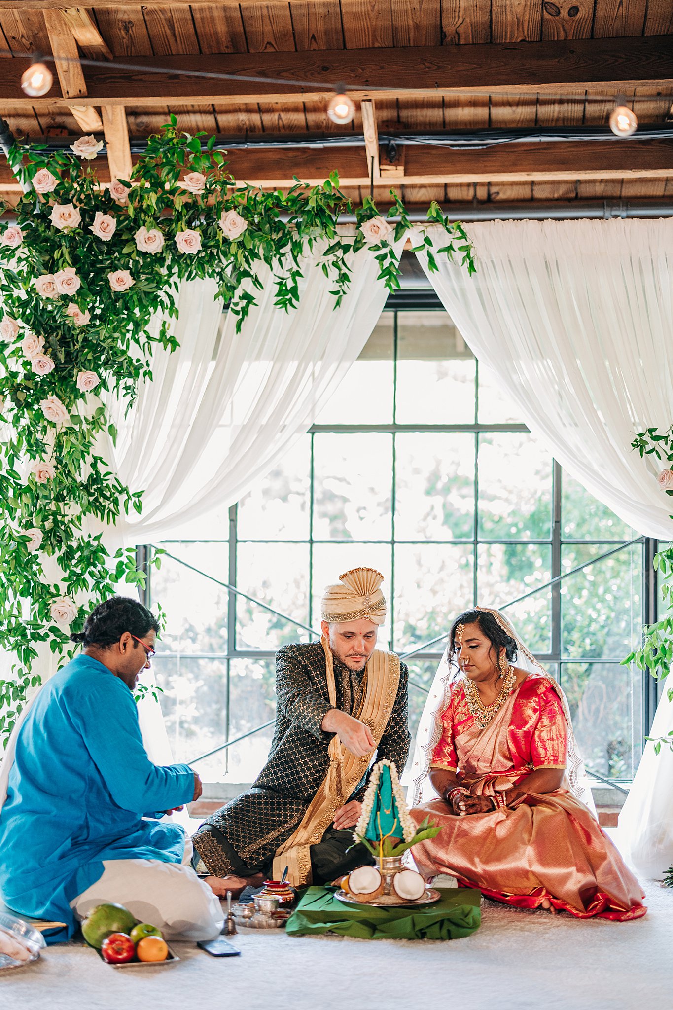 A bride and groom partake in their traditional wedding ceremony while sitting under pink roses
