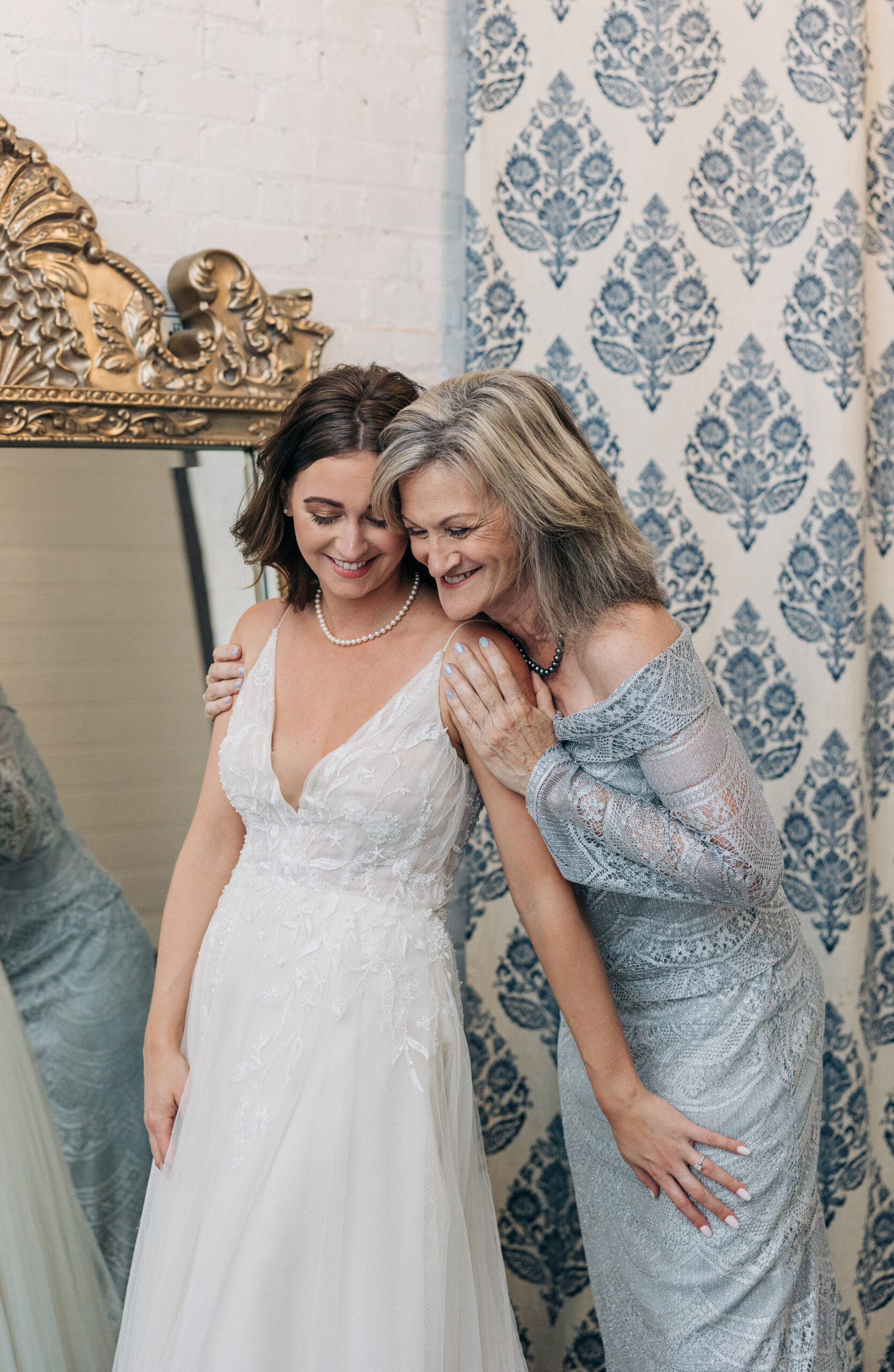 A mother in a blue lace dress smiles big while hugging her daughter in her Providence Cotton Mill wedding dress