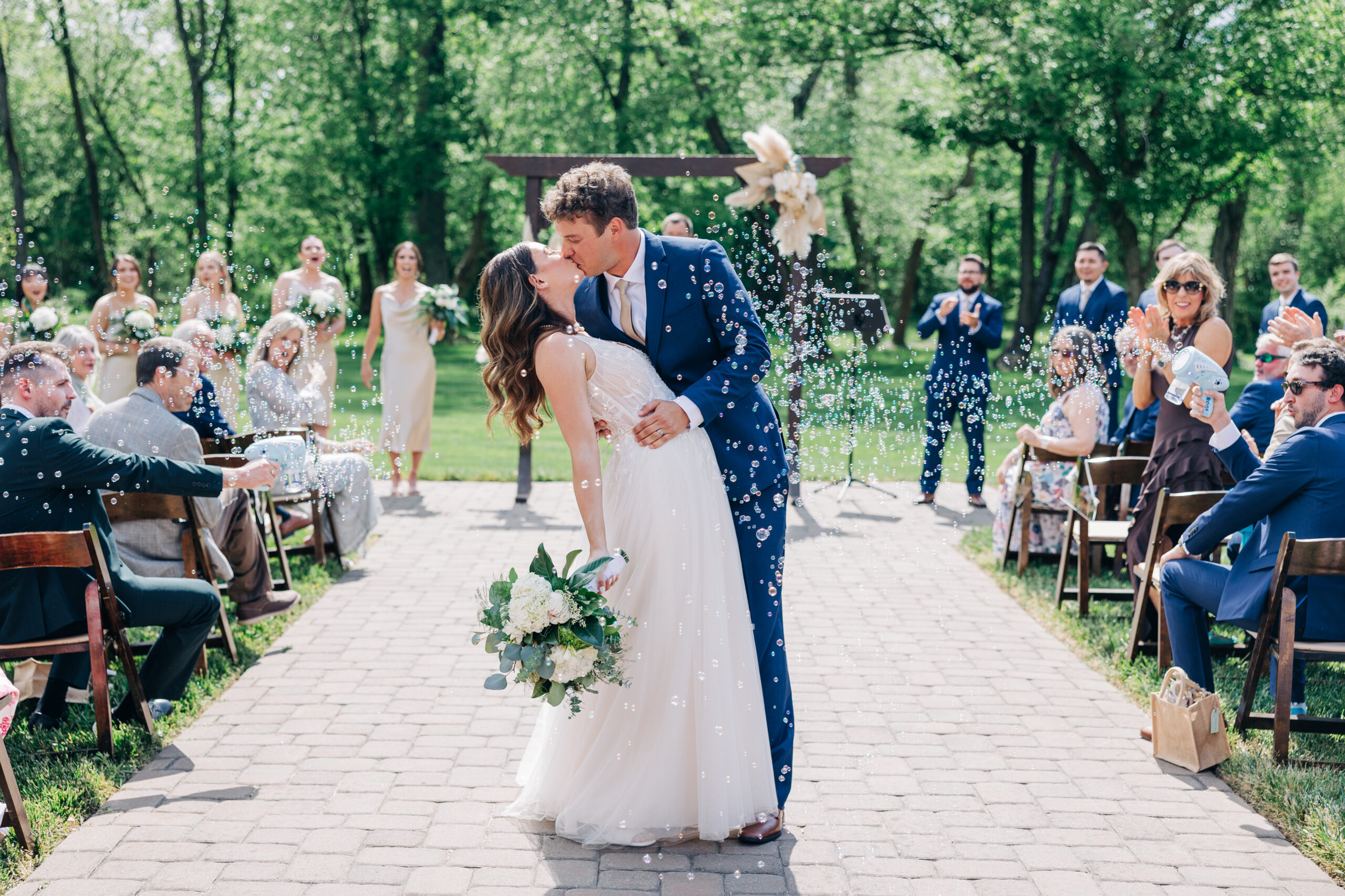 Newlyweds kiss under a shower of bubbles while walking up the aisle of their outdoor Providence Cotton Mill wedding ceremony