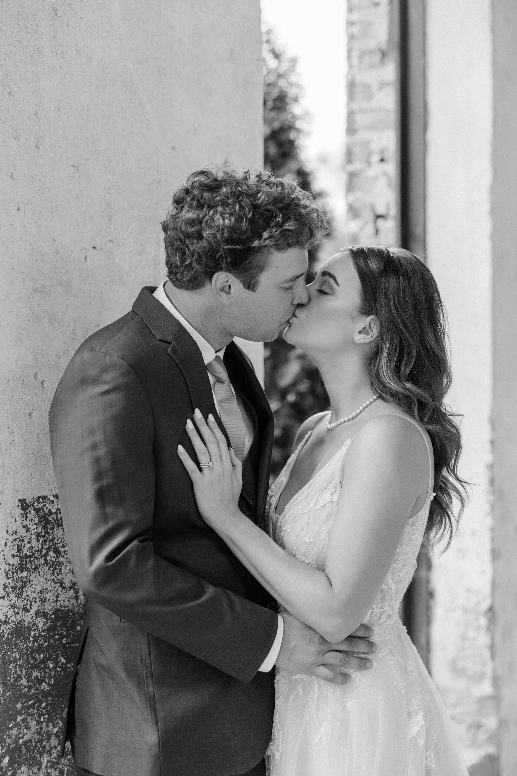 Newlyweds lean on a rustic wall while kissing