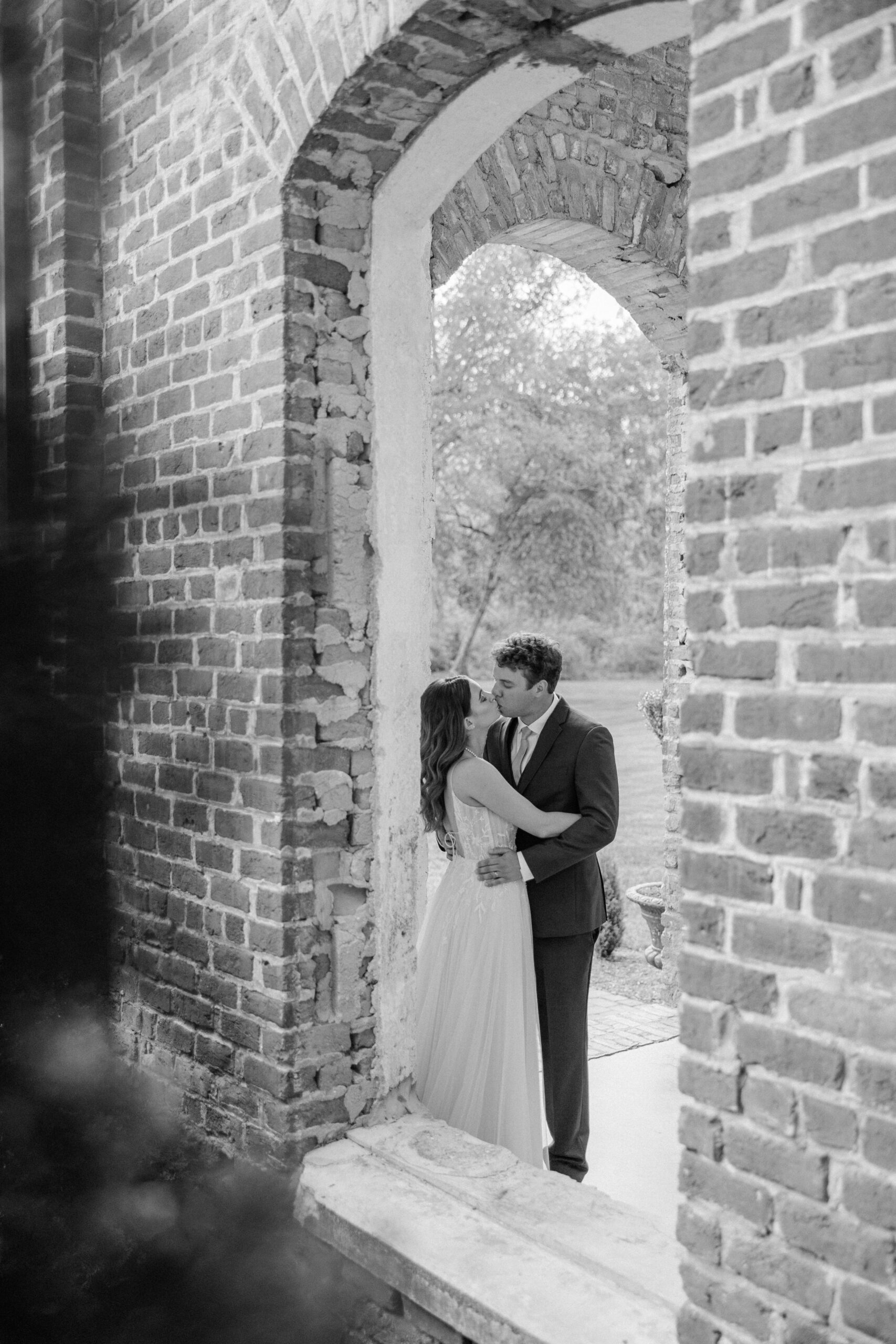 Newlyweds share an intimate kiss through a window on the patio of their brick wedding venue