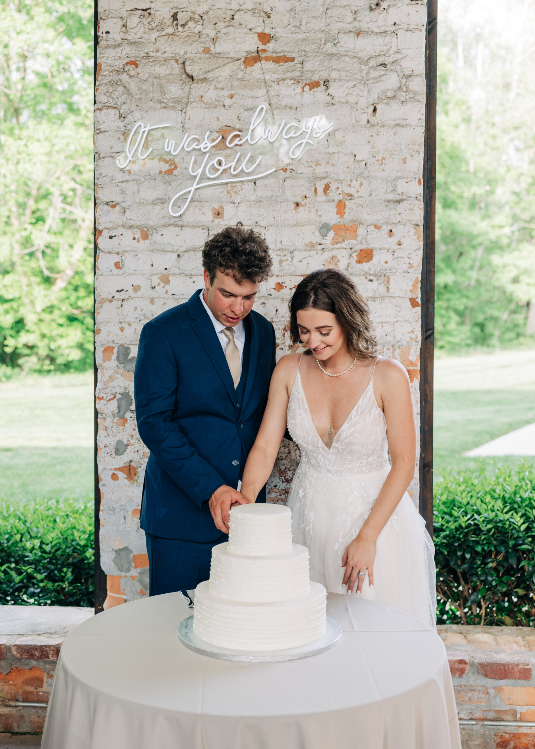 Newlyweds cut their white three tier cake in a lace dress and blue suit