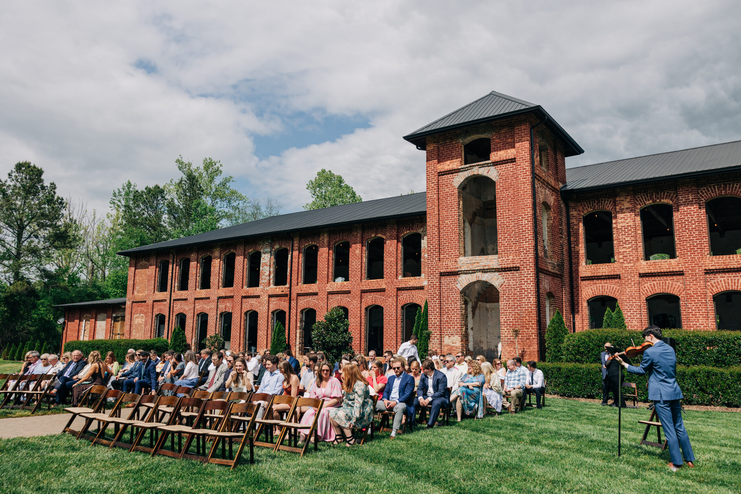 A view of a violin player performing as guests wait for an outdoor Providence Cotton Mill wedding ceremony to start