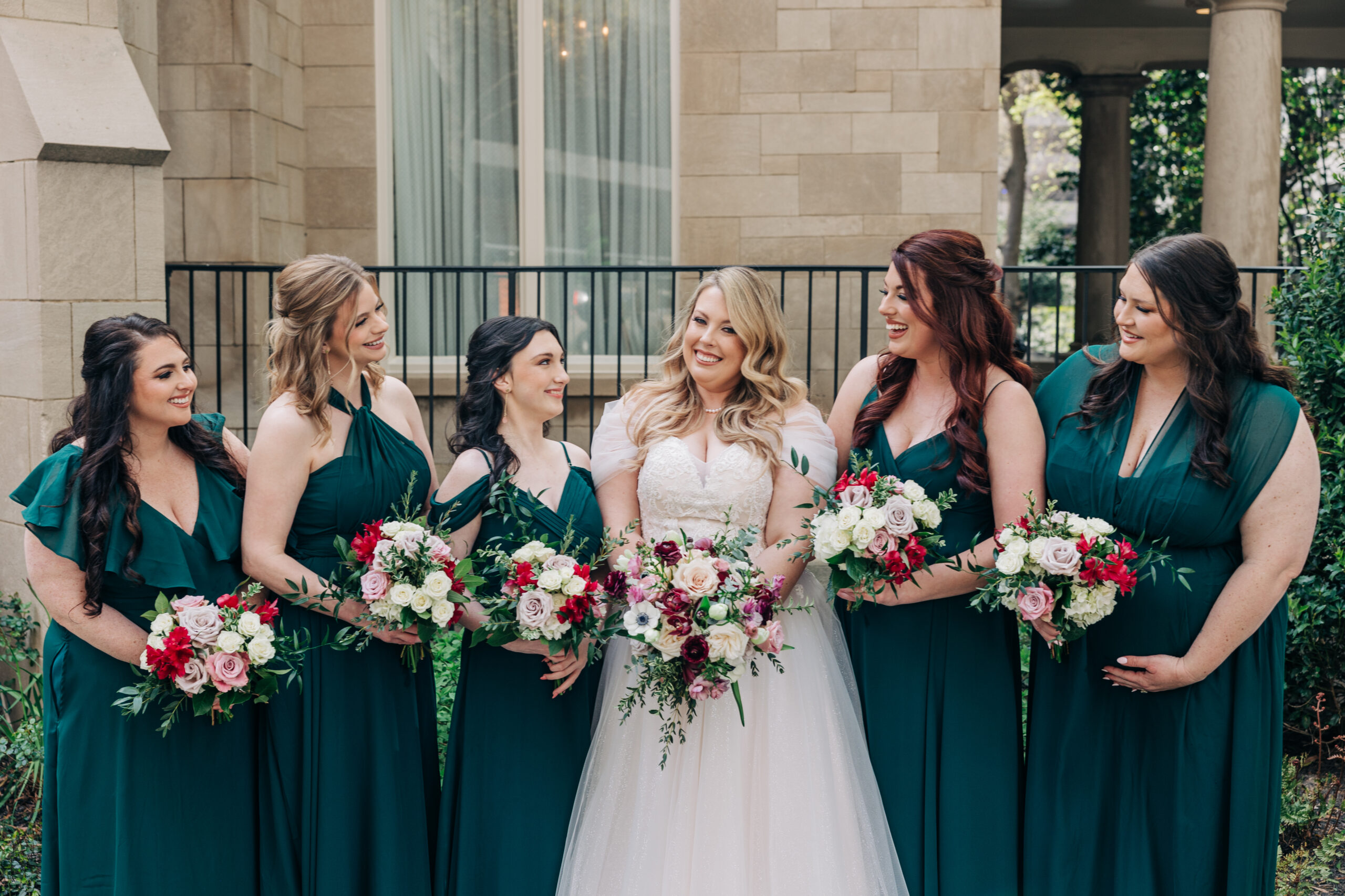A bride smiles big while her bridesmaids smile at her and hold their bouquets