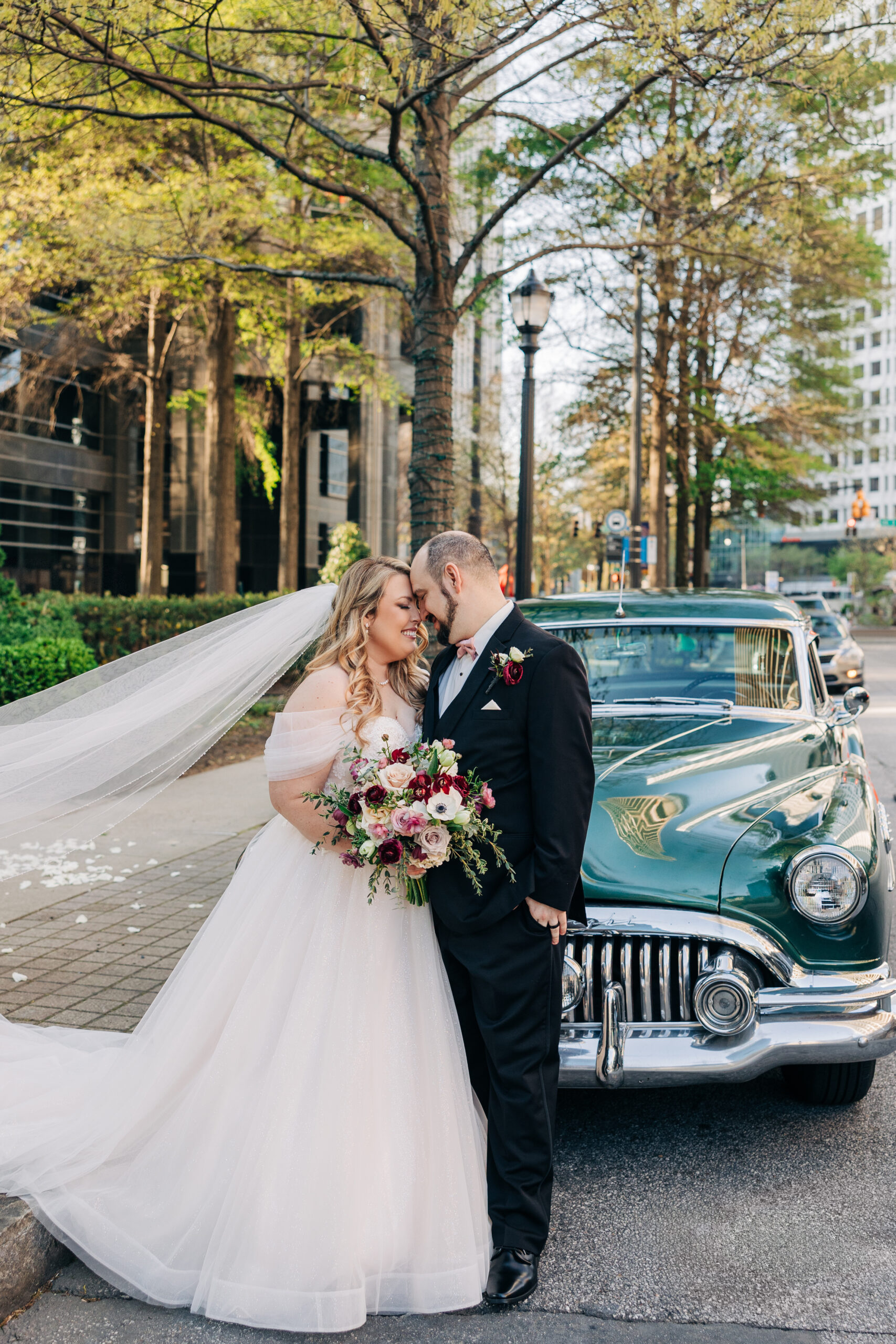 Newlyweds stand on the street in front of the Wimbish House wedding venue and a vintage green car while touching foreheads