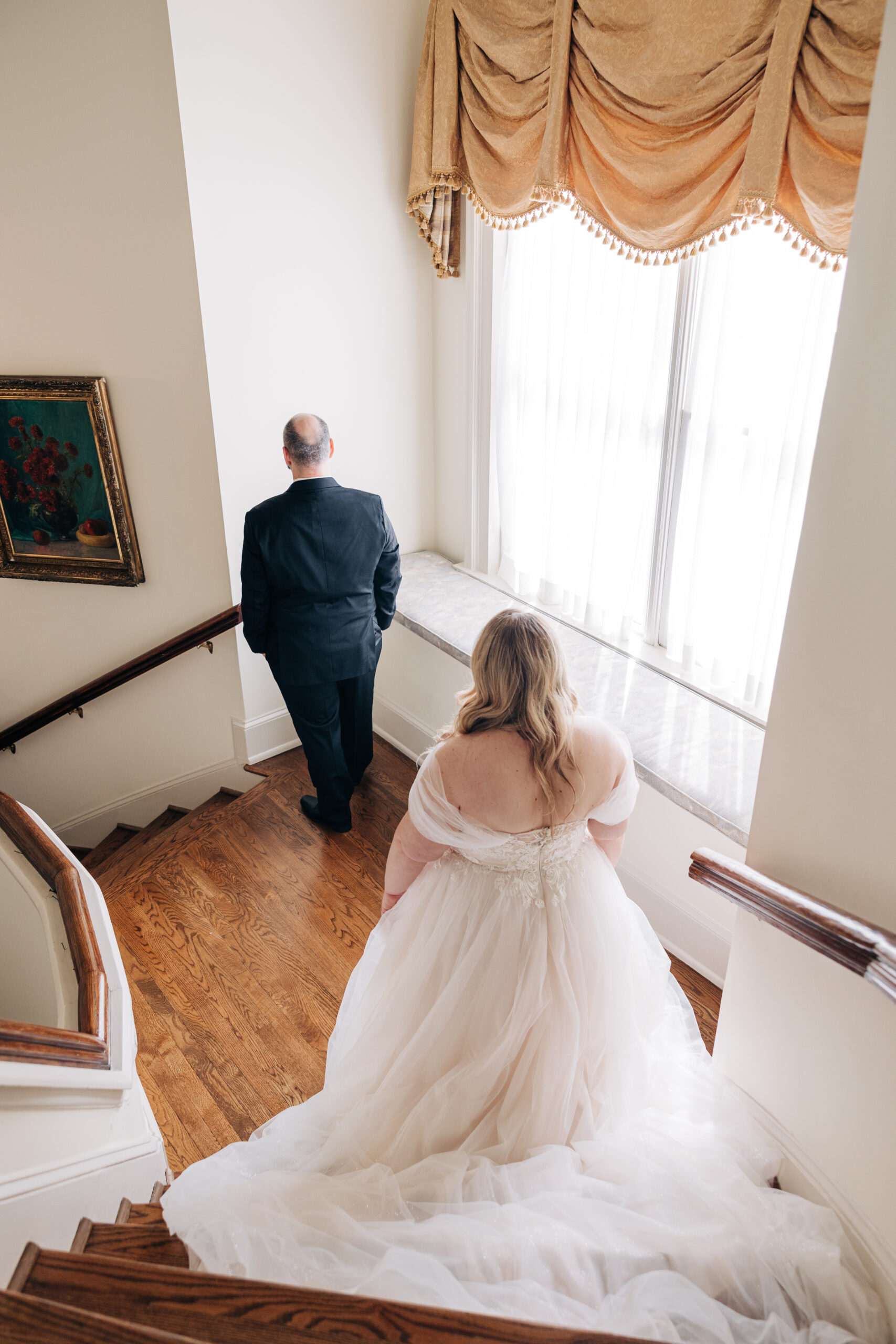 A groom waits on a stair landing as his bride prepares for their first look