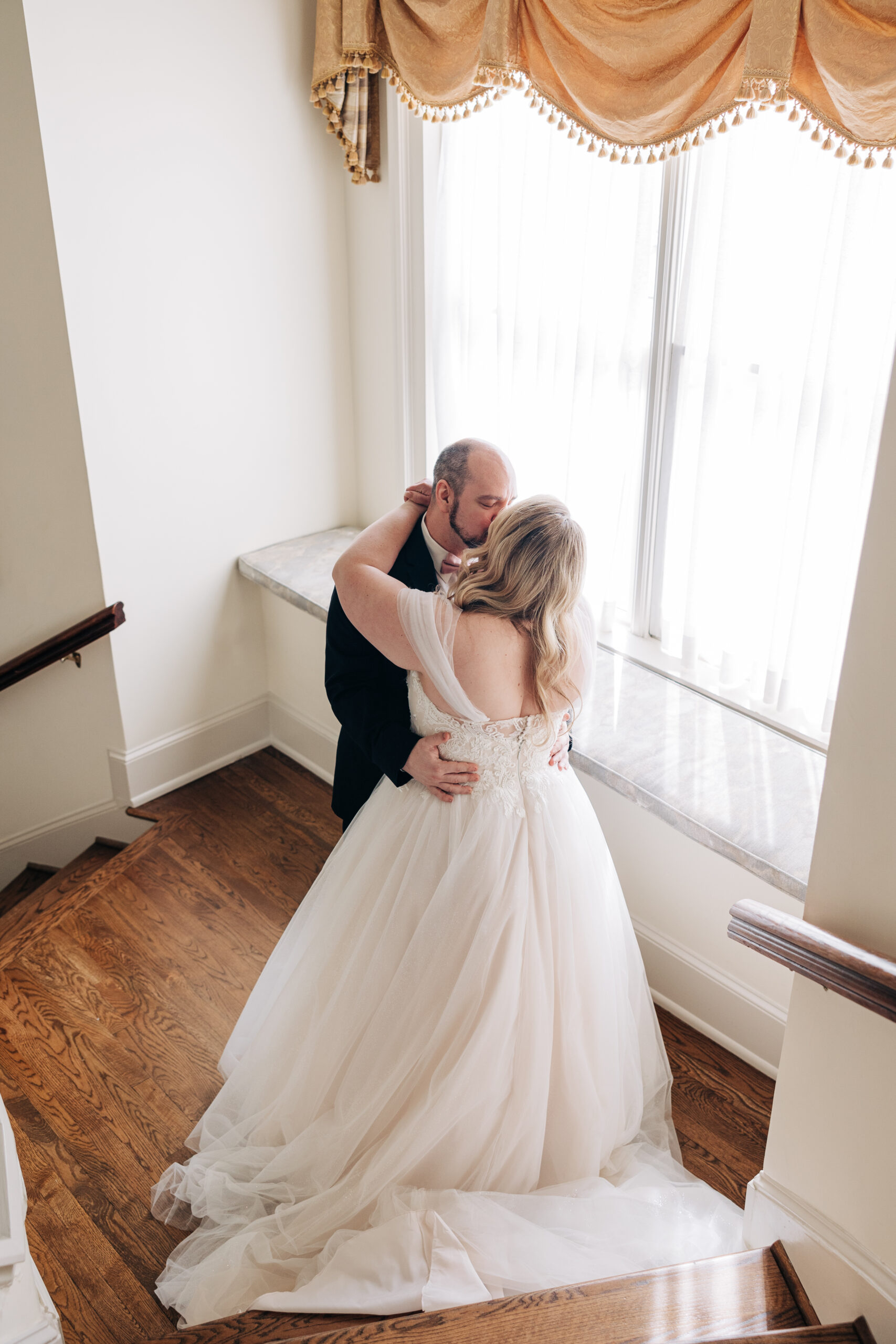 Newlyweds kiss while standing in a stair landing in a window during their first look at their Wimbish House wedding