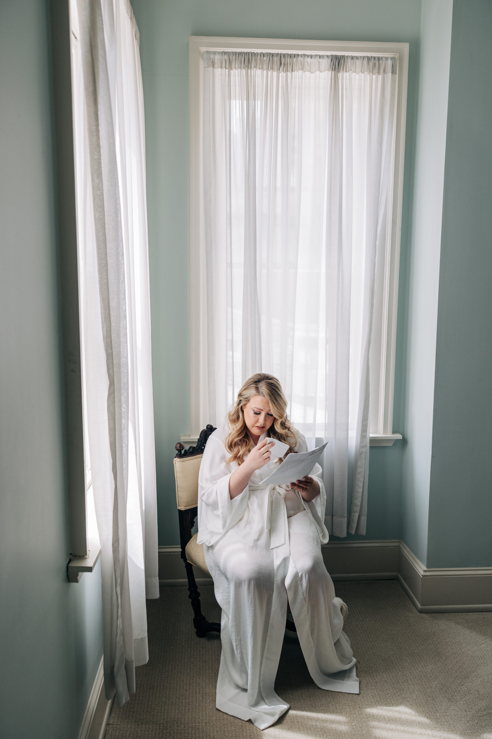 A bride cries while reading a letter and sitting in a chair in a robe