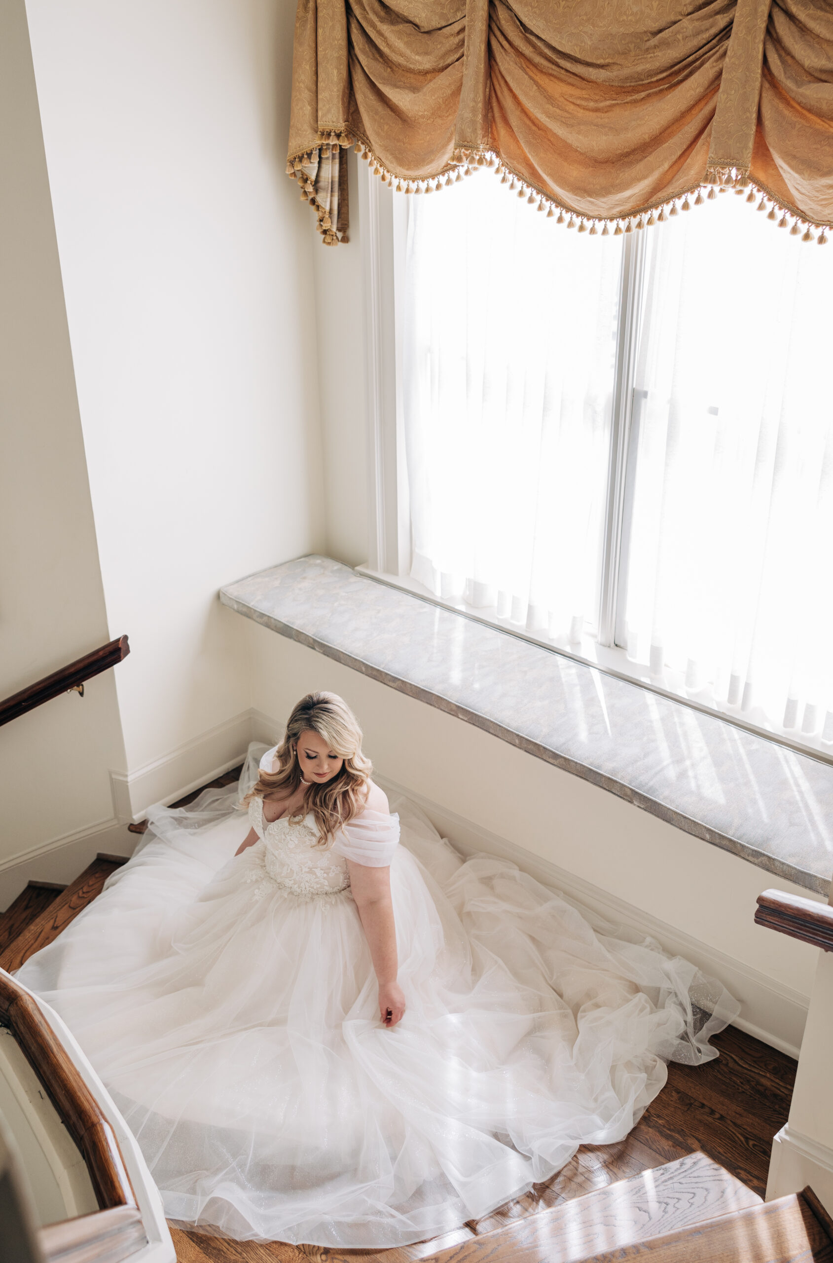 A bride sits surrounded by her long train in a large stairway landing at her Wimbish House wedding