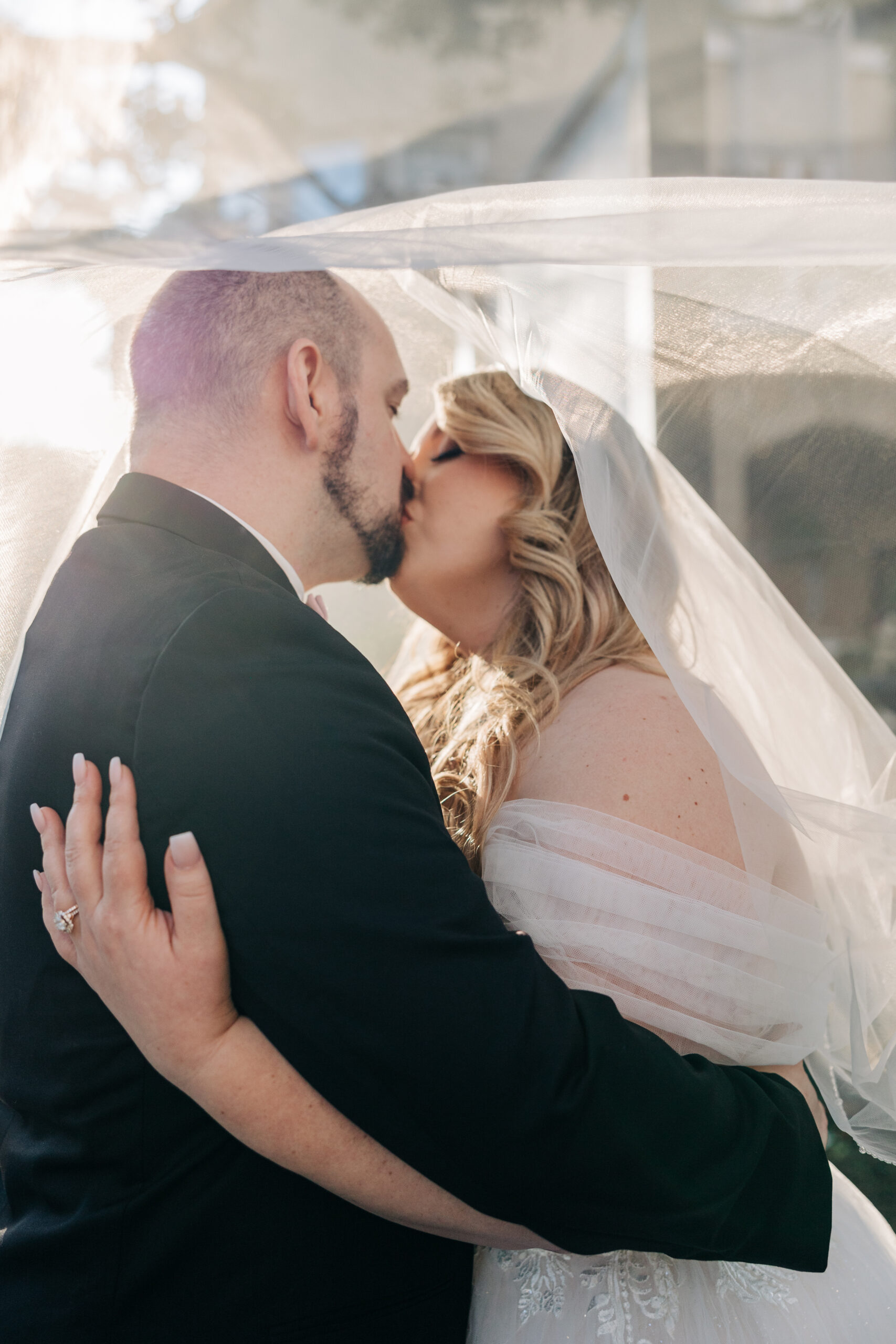 Newlyweds share a kiss while hiding under the veil outside at sunset