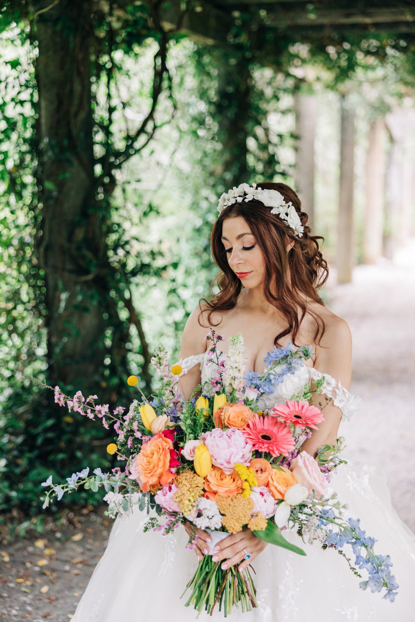 A bride walks and looks down at her large bouquet of colorful flowers