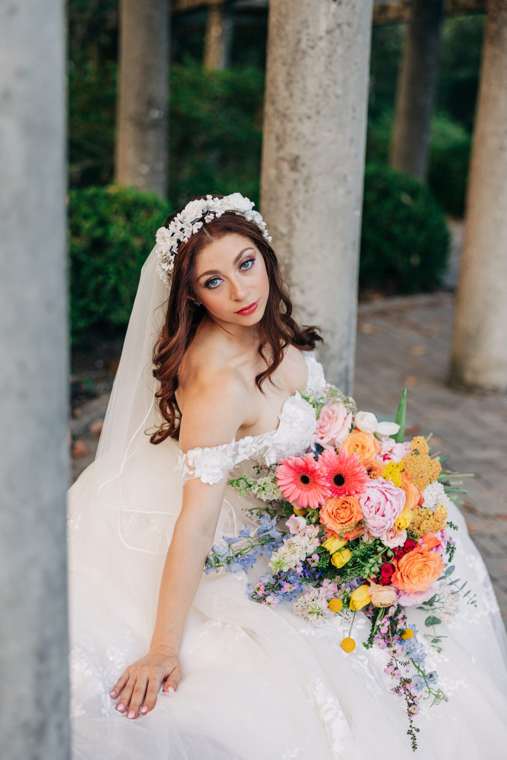 A bride sits on a bench with her bouquet in her lap in a gazebo